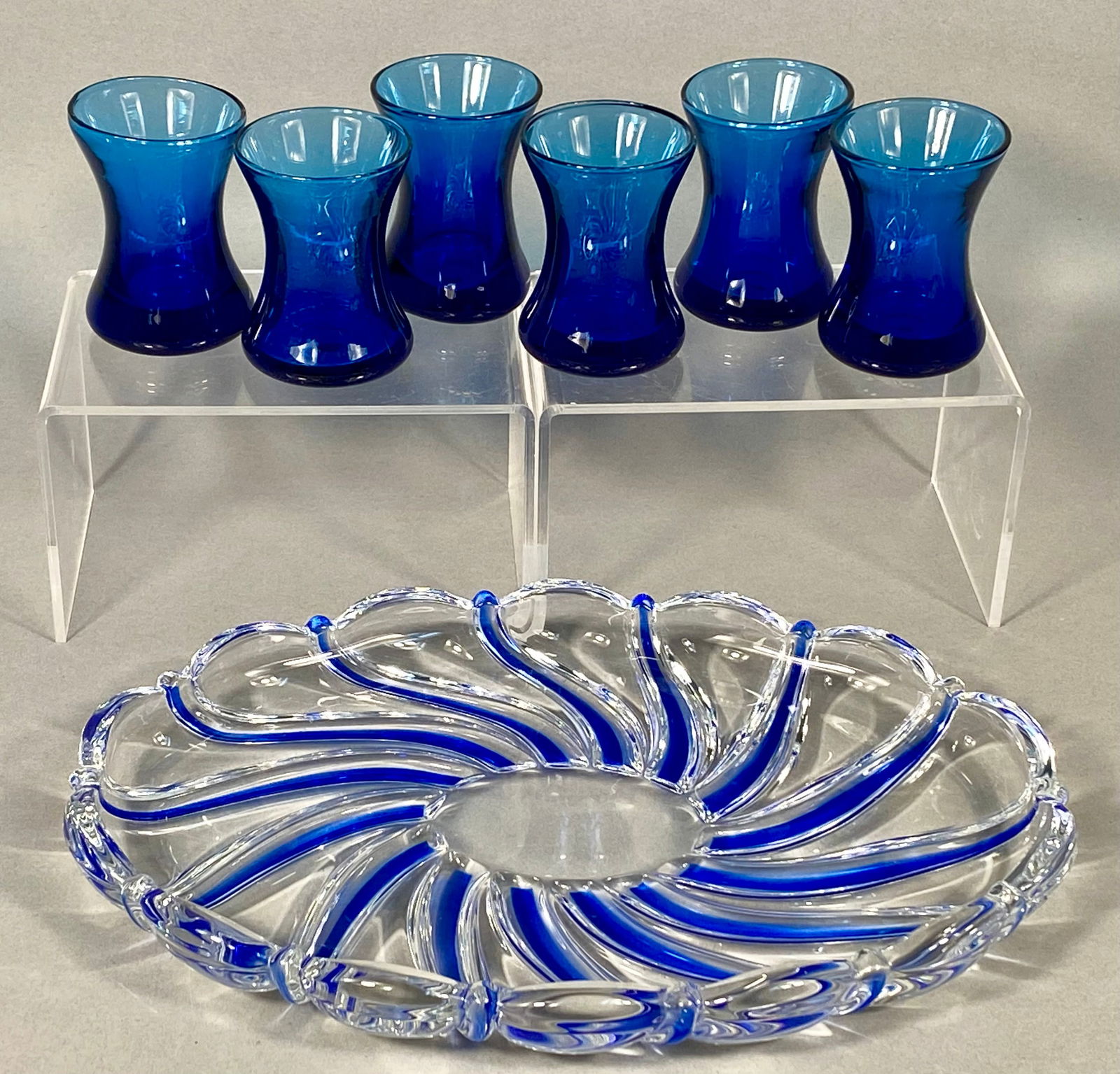 Mikasa Peppermint Cobalt Swirl Platter and Six Cobalt Shot Glasses: The platter is attributed to Mikasa in the Peppermint Cobalt pattern. It is constructed of clear molded or pressed glass, distinguished by a wide, scalloped rim and an internal decorative motif of spi