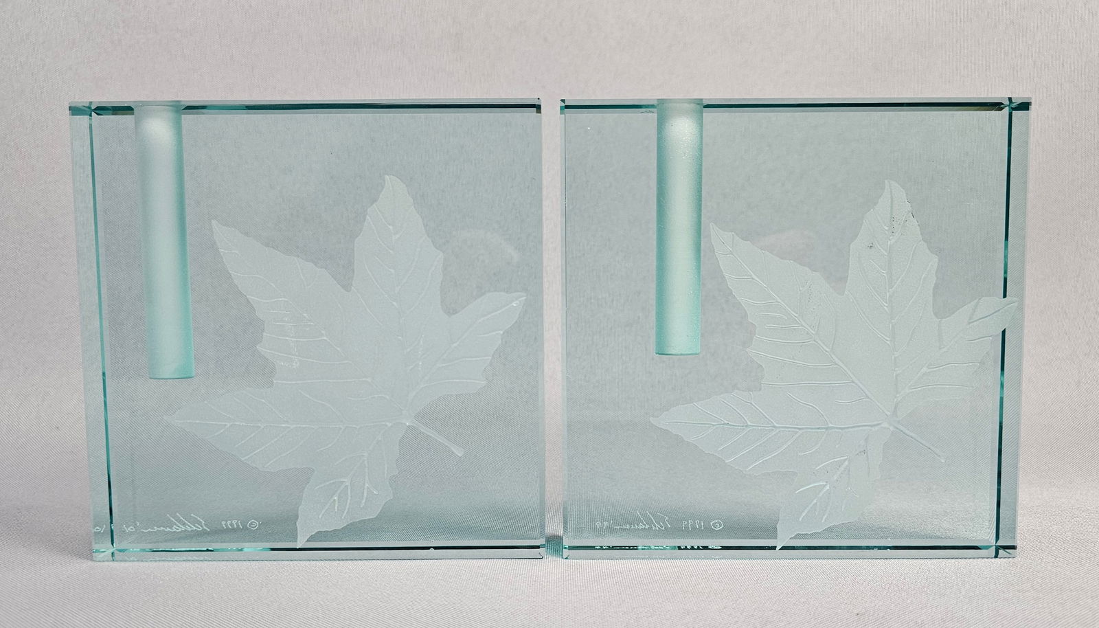 A Pair of Signed Stephen Schlanser Etched Art Glass Leaf Bud Vases: A pair of contemporary art glass bud vases attributed to Stephen Schlanser. Each piece is constructed from a thick, polished rectangular block of light teal-tinted glass. A central, vertical, frosted