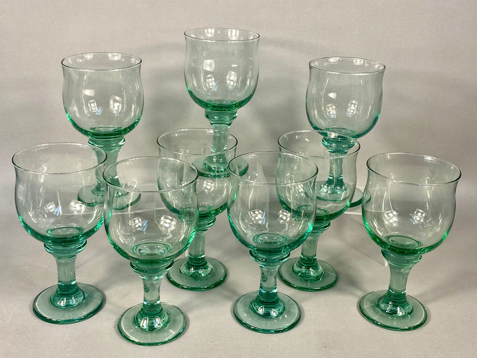 A Set of Libbey Clarion Spanish Green Glass Goblets: A set of nine glass water goblets produced by Libbey in the Clarion pattern and Spanish Green colorway. Each piece features a rounded, bulbous bowl with a slightly flared rim, supported by a thick, ta