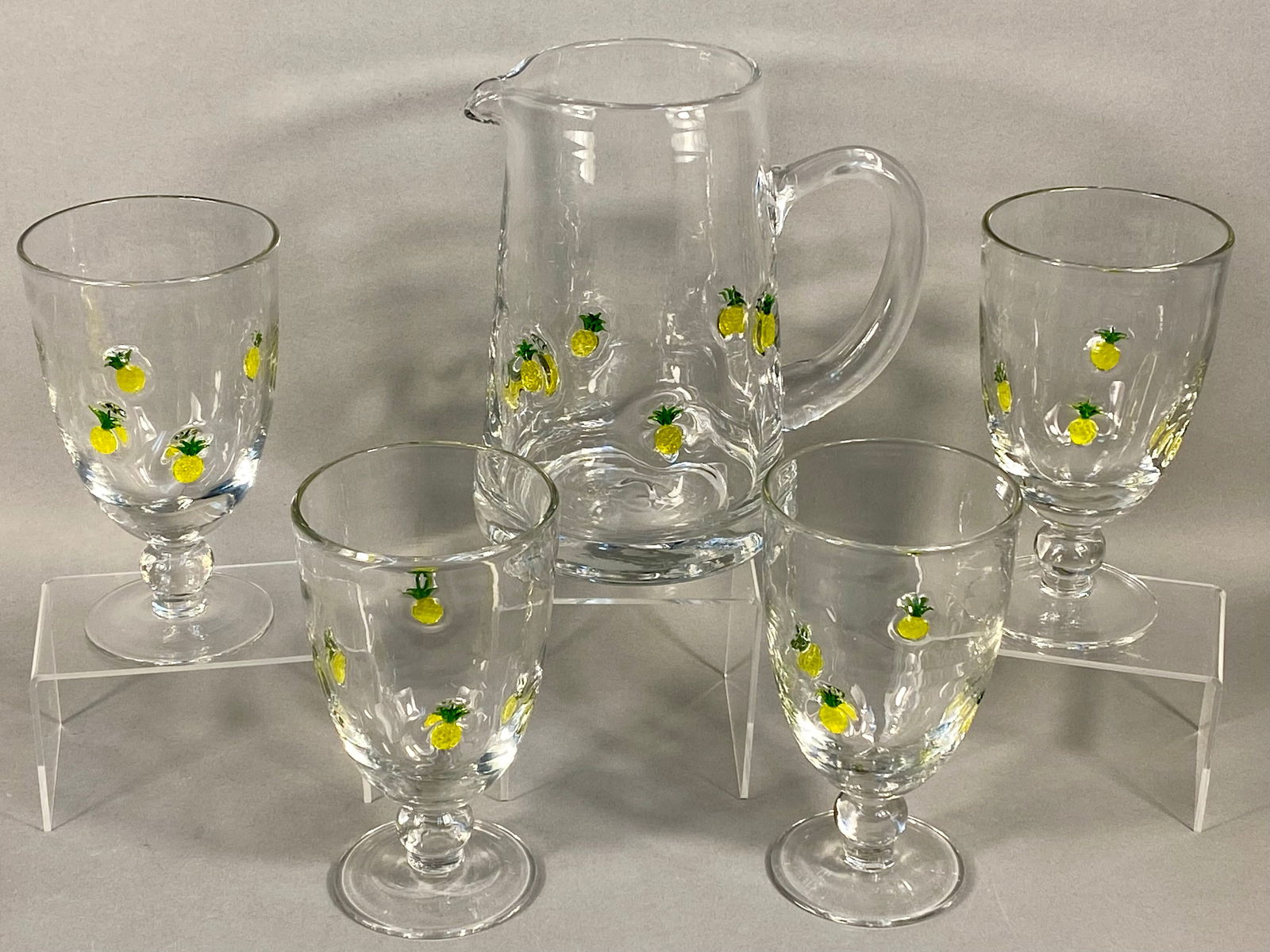 Artland Pineapple Welcome Pattern Glass Beverage Set: A set of Artland Pineapple Welcome pattern glassware. This collection is hand-blown from clear glass featuring a wavy, hammered texture. Each piece is decorated with multiple applied yellow and green