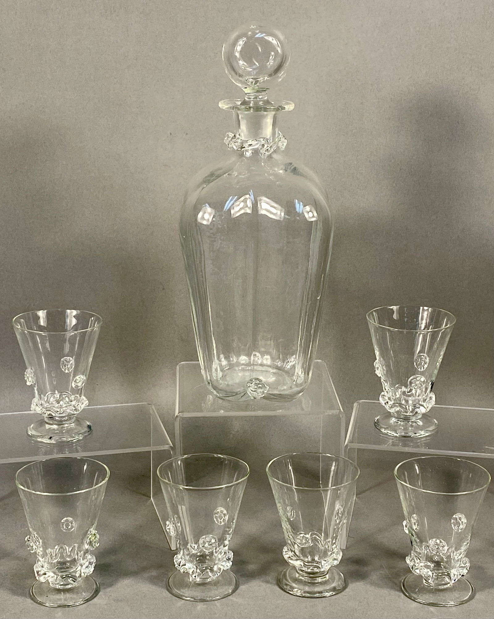 A Set of Iittala Ryppy Glass Tableware Designed by Erkki Vesanto: A set of hand-blown clear glass tableware in the Ryppy pattern, designed by Erkki Vesanto for Iittala. The collection includes a decanter with a matching spherical stopper and four footed glasses. The