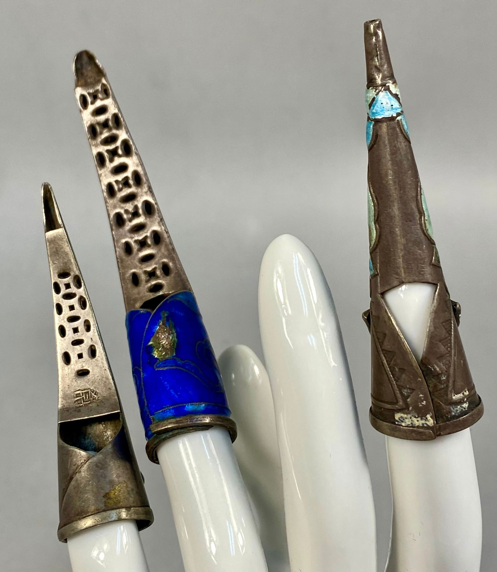 A Trio of Antique Chinese Silver and Enamel Finger Nail Guards: This trio of antique Chinese silver and enamel finger nail guards features various traditional motifs and decorative techniques. The collection includes one guard with cobalt blue cloisonne enamel dep
