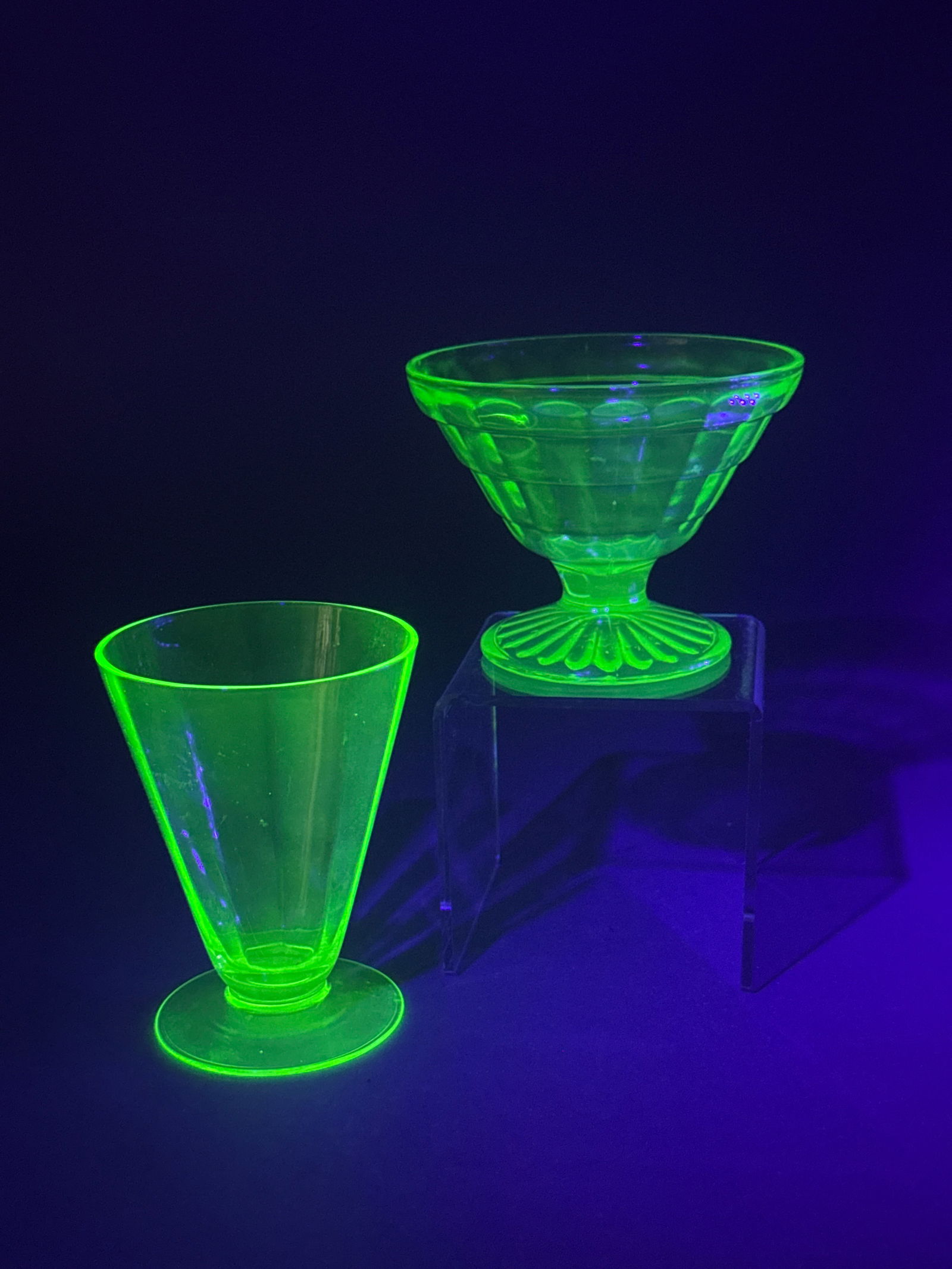 Two Pieces of Depression Era Uranium Glass: This lot features two pieces of pale green uranium glass, which exhibit a characteristic bright green fluorescence under ultraviolet light. Included is a sherbet or dessert cup featuring a paneled, st