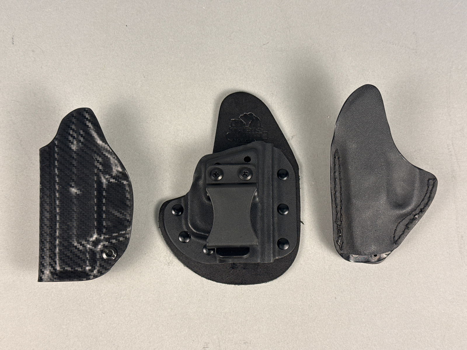 A Trio of Modern Handgun Holsters including Theis Holsters: A trio of modern handgun holsters featuring a hybrid IWB model by Theis Holsters, similar in design to the Crossbreed SuperTuck series. The Theis holster is constructed with a textured leather backing