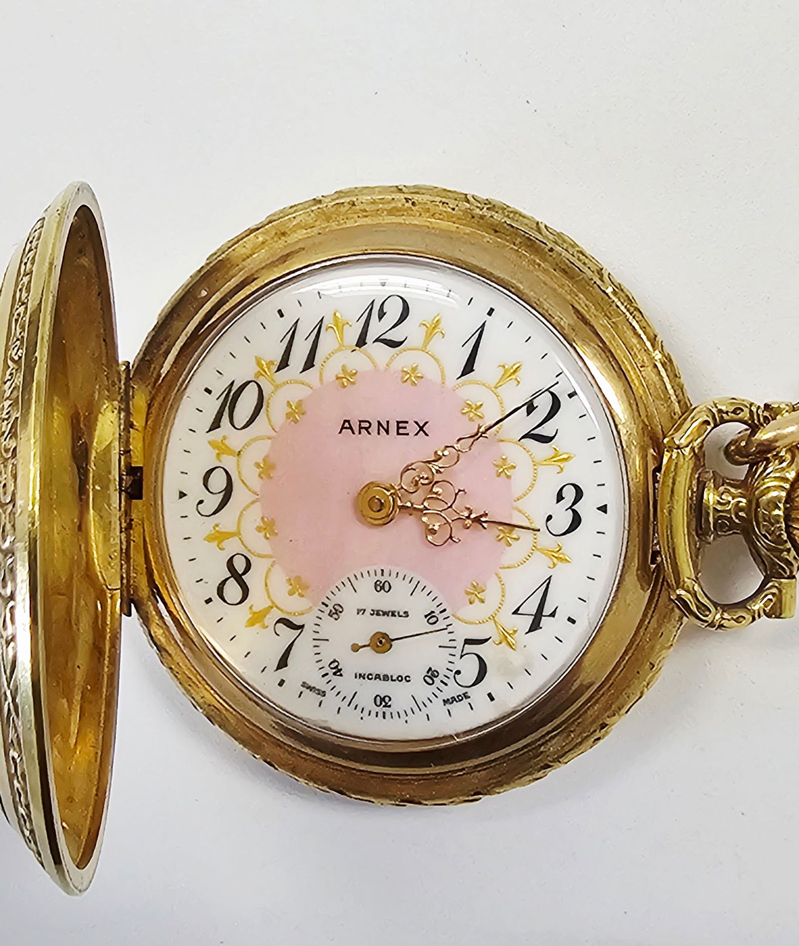 Arnex Vintage Swiss 17 Jewel Pocket Watch with Chain: This Arnex vintage hunter-case pocket watch features an ornate gold-plated case with intricate scrolled and rayed engraving on both the front and back covers. The decorative white dial is designed wit