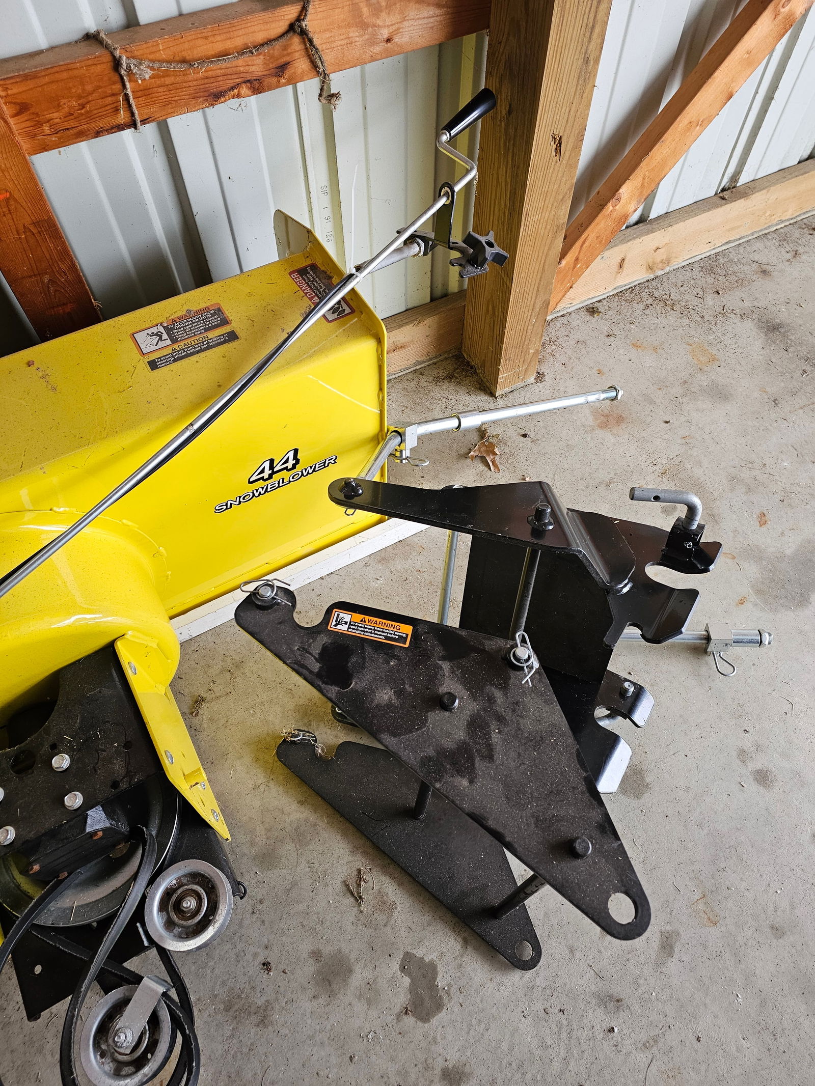 John Deere 44-inch Snow Blower Attachment: A John Deere Model 44-inch snow blower attachment, manufactured on October 13, 2018. The unit is constructed from yellow and black painted steel with a black plastic discharge chute. The design featur
