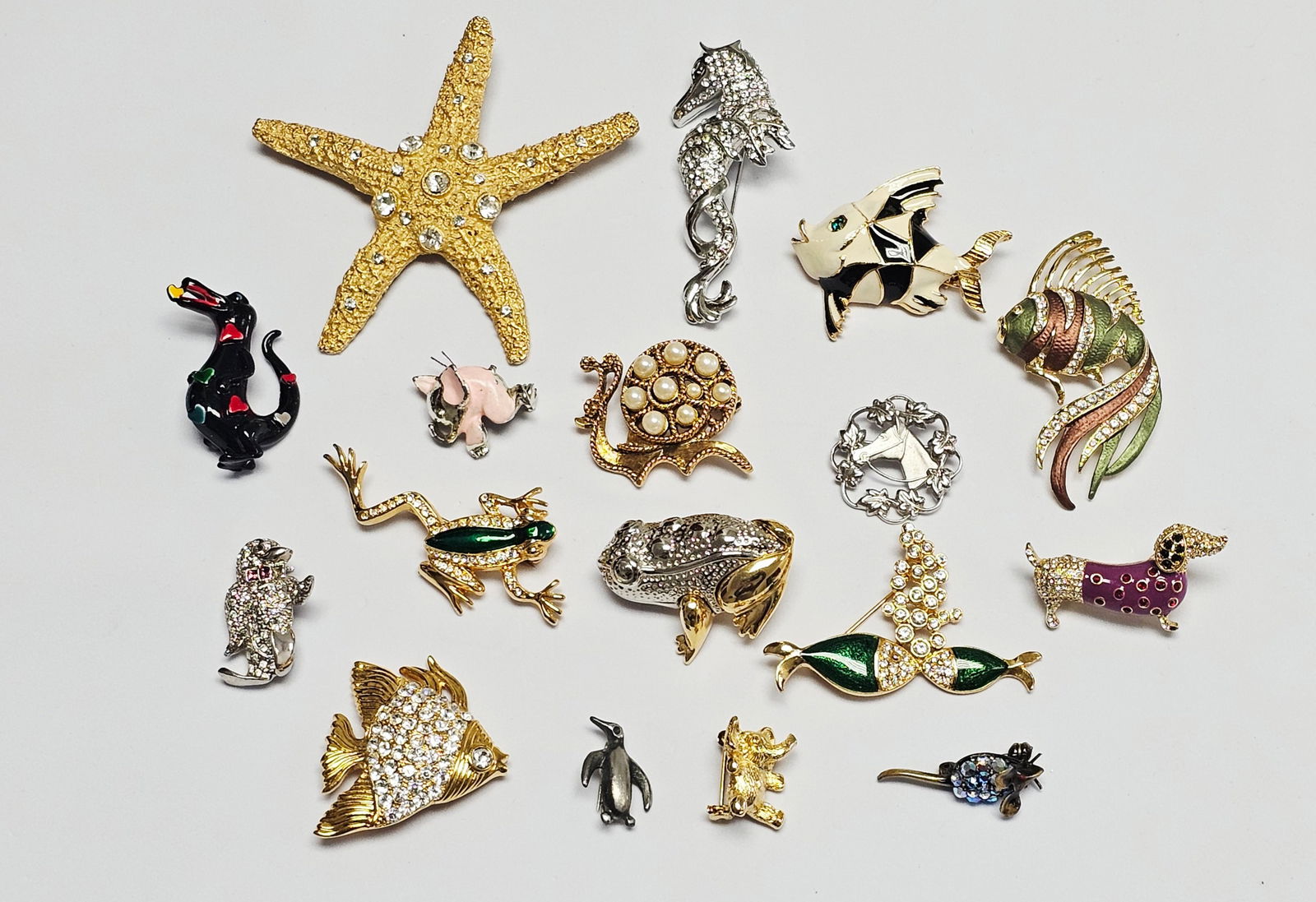 Animal and Marine Motif Costume Jewelry Brooches: This collection of costume jewelry brooches features various animal and marine life motifs, including a large gold-tone textured starfish brooch attributed to Carolee. The starfish is accented with