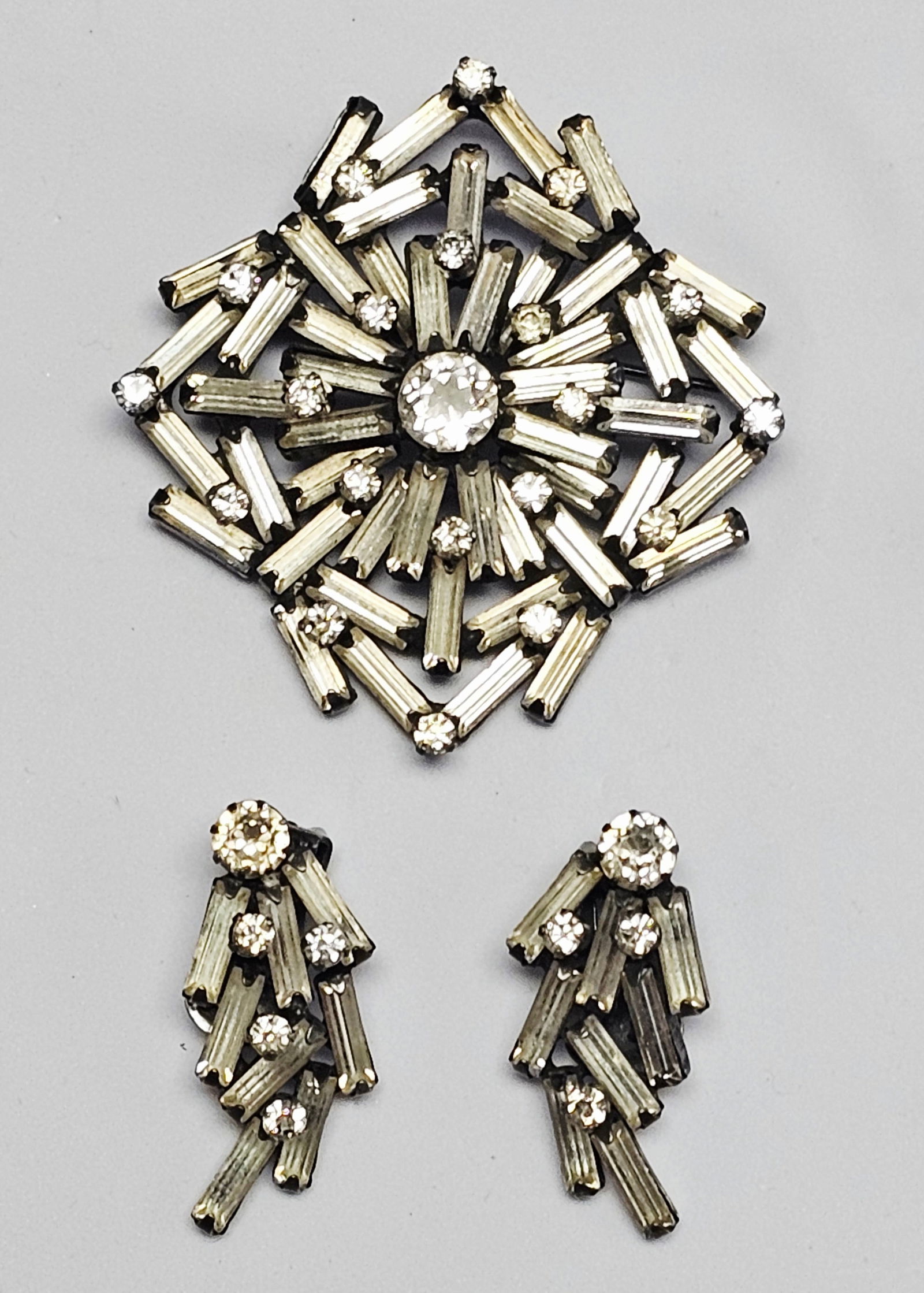 Vintage Weiss Emerald Cut and Round Clear Rhinestone Brooch & Earrings: A trio of vintage Weiss jewelry featuring emerald cut and round clear rhinestones. The set consists of a brooch and a pair of coordinating clip-on earrings. Each piece is constructed from silver-tone