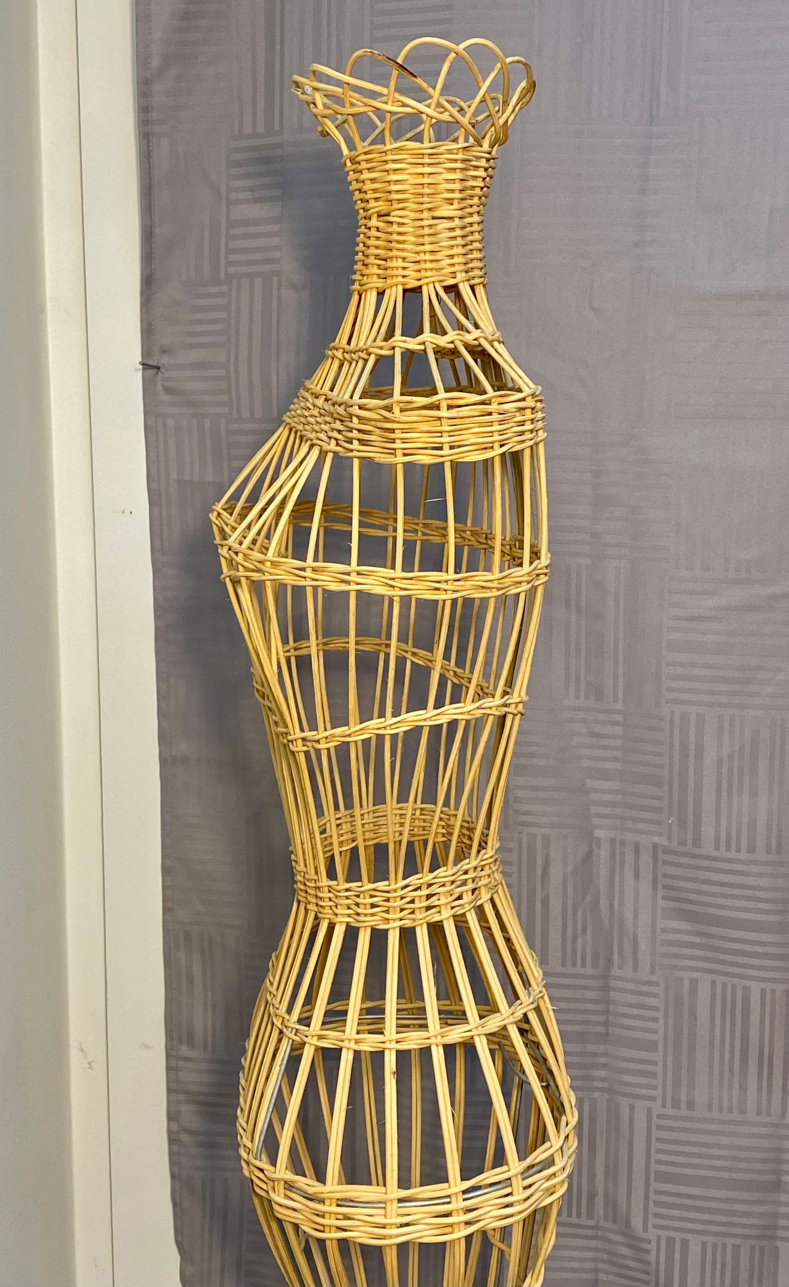 A Vintage Wicker Dress Form Mannequin: A vintage dressmaker mannequin constructed from woven wicker and rattan in a light natural finish. The piece features a hollow, open-cage design following a feminine silhouette with a defined bust and