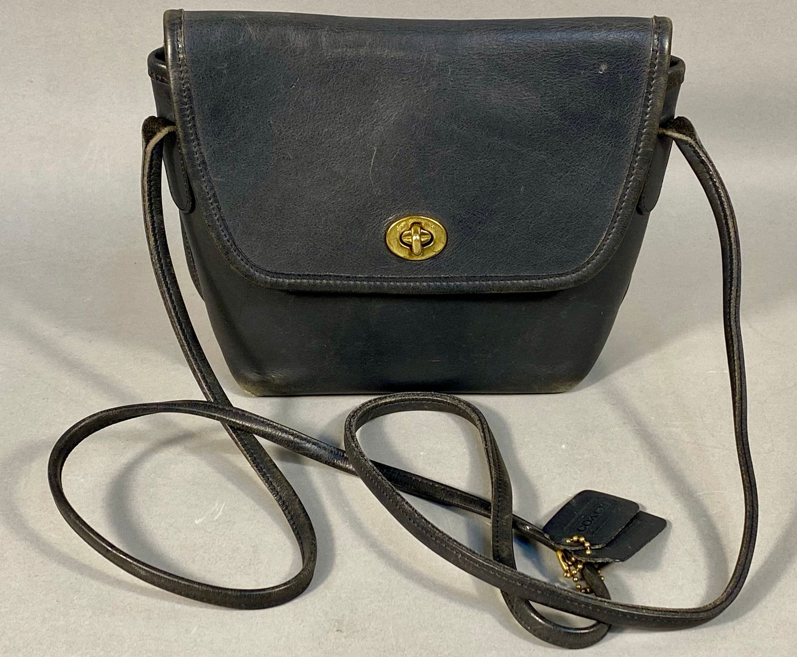 Vintage Coach Quincey Leather Crossbody Bag 9919: A vintage Coach Quincey crossbody bag, model number 9919. This bag is constructed from dark navy blue glovetanned leather and features a front flap with a brass-tone metal turnlock closure. The design