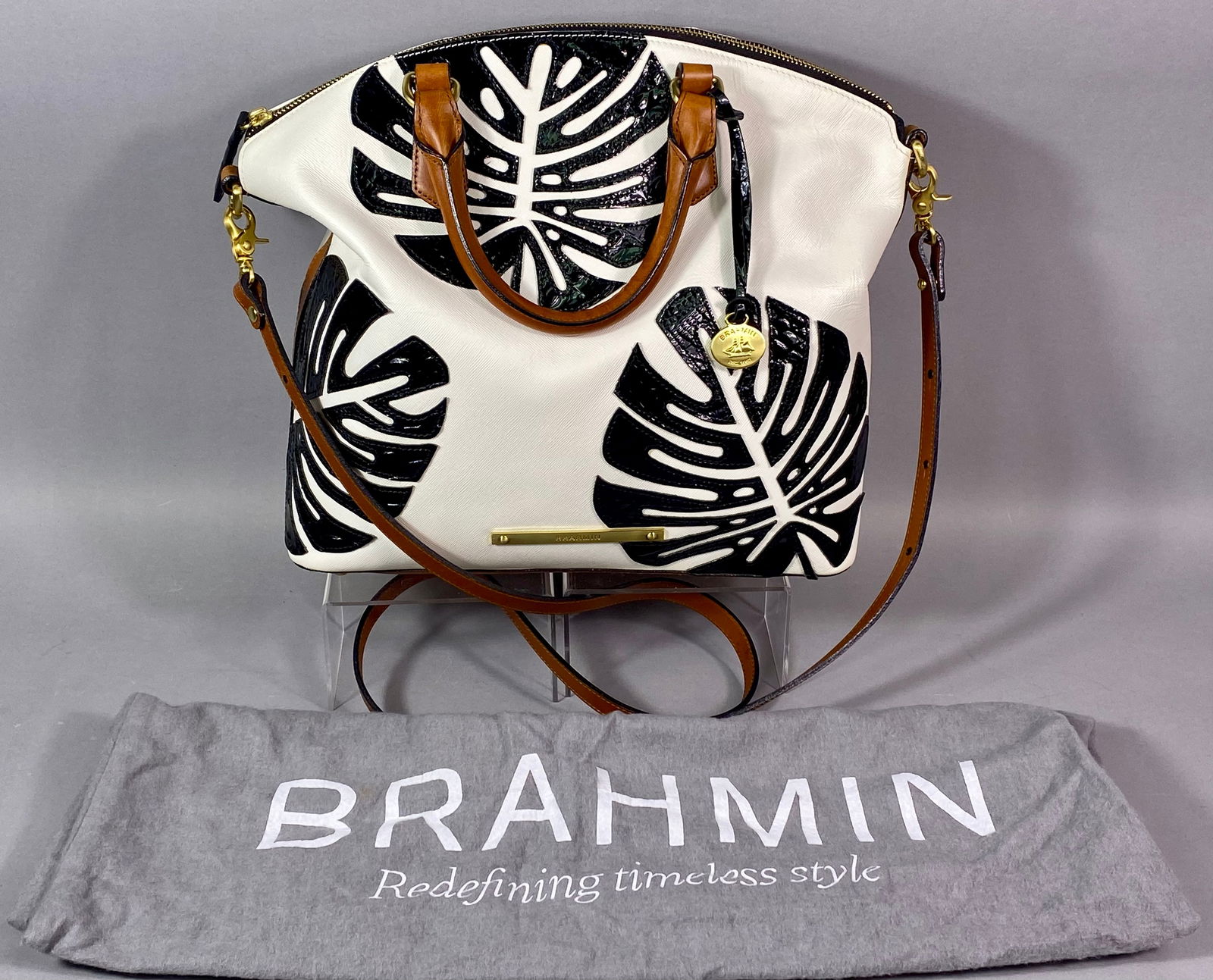 Brahmin Large Duxbury Satchel with Palm Leaf Applique: A Brahmin Large Duxbury satchel featuring a textured white leather exterior decorated with three large black patent leather monstera leaf appliqués. The bag is constructed with smooth brown lea