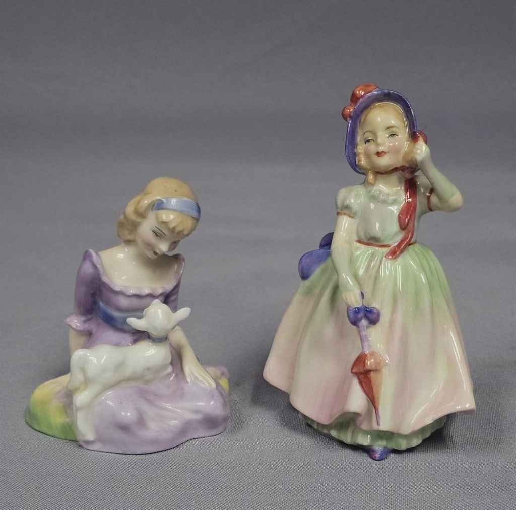 Two Royal Doulton Porcelain Figurines Mary Had a Little Lamb HN 2048 and Babie HN 1679: Two hand-painted bone china figurines produced by Royal Doulton. The first figurine, titled Mary Had a Little Lamb (model HN 2048), depicts a seated girl in a lavender dress with a blue sash and headb