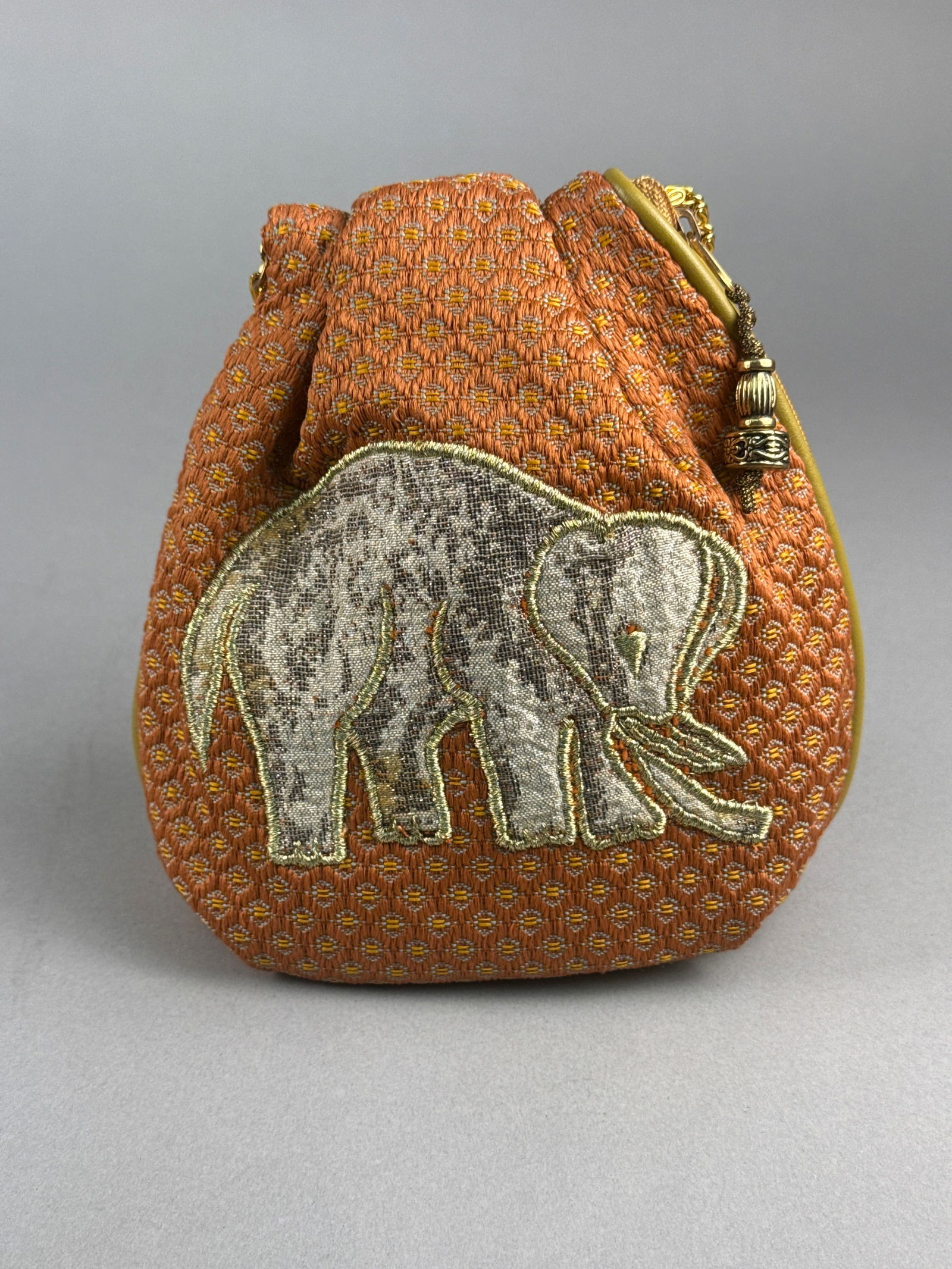 A Shin Sai Bashi Kalaga Style Embroidered Elephant Pouch Evening Bag: A Japanese pouch-style evening bag produced by Shin Sai Bashi of Tokyo. The bag is crafted from an orange and gold patterned woven fabric featuring a large stylized elephant in metallic silver and