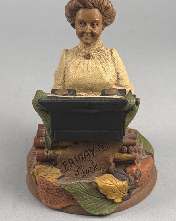 Tom Clark Cairn Studio Friday Gnome Figurine, 1990: A Tom Clark gnome figurine titled Friday, produced by Cairn Studio in 1990. The cast resin piece depicts a female figure wearing a green conical hat and a cream-colored textured top, seated at a black