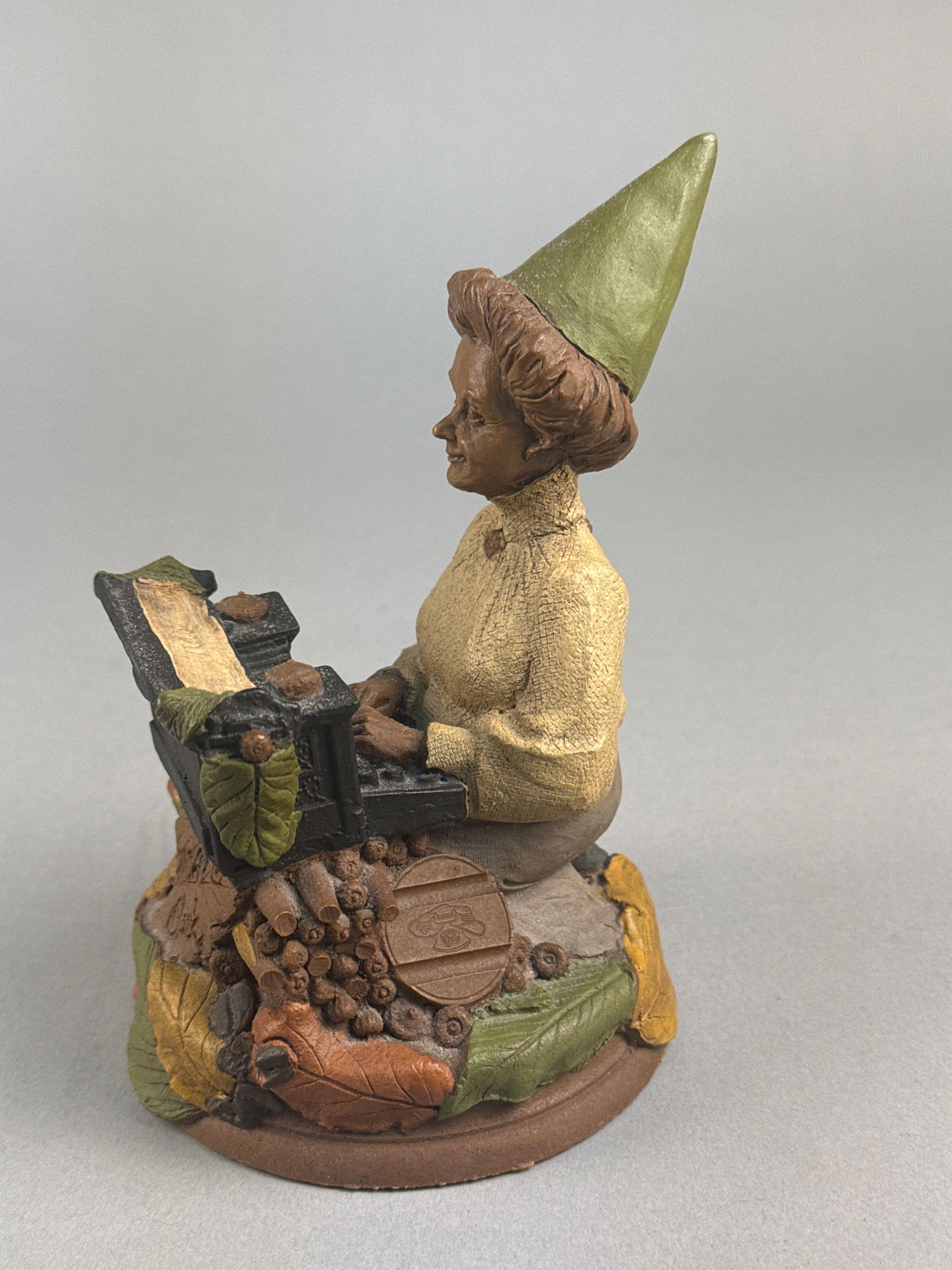 Tom Clark Cairn Studio Friday Gnome Figurine, 1990: A Tom Clark gnome figurine titled Friday, produced by Cairn Studio in 1990. The cast resin piece depicts a female figure wearing a green conical hat and a cream-colored textured top, seated at a