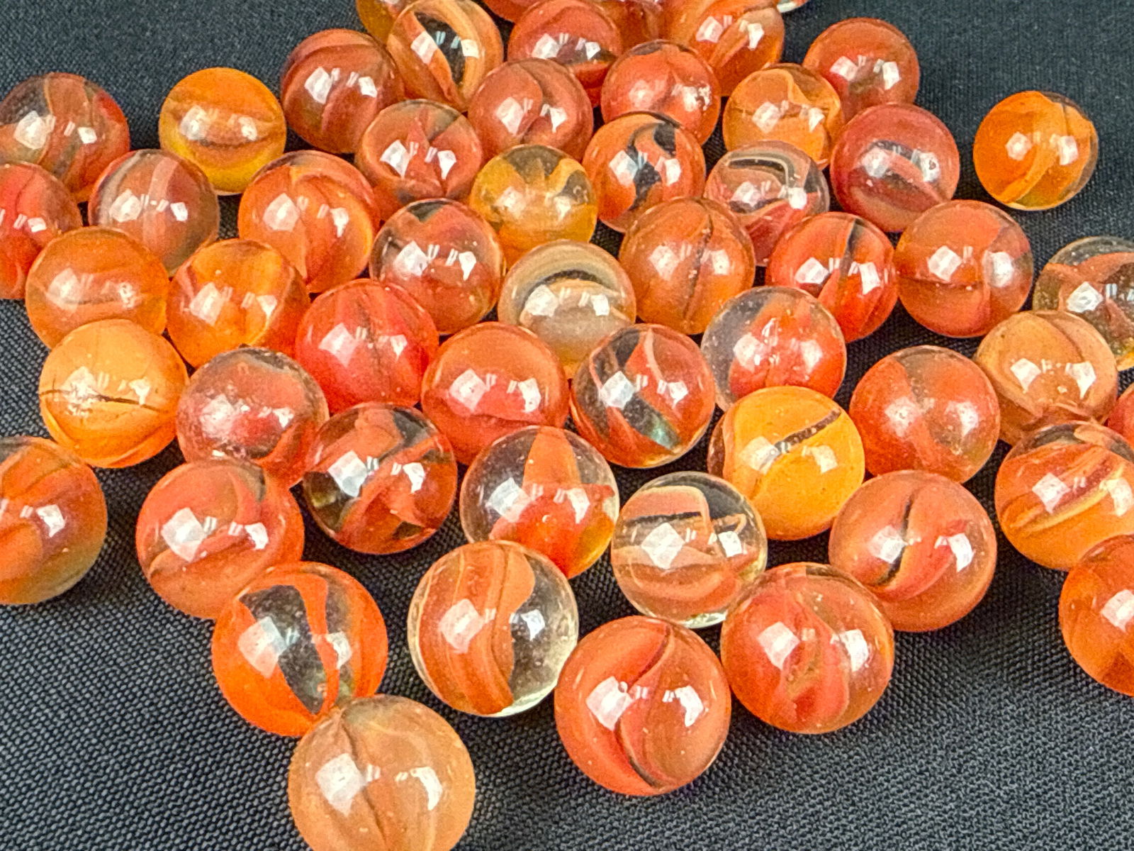 A Collection of Red Cat's Eye Glass Marbles: A collection of glass marbles featuring a cat's eye pattern. Each specimen is constructed of transparent clear glass containing internal multi-vane swirls in shades of orange, red, and dark brown. The
