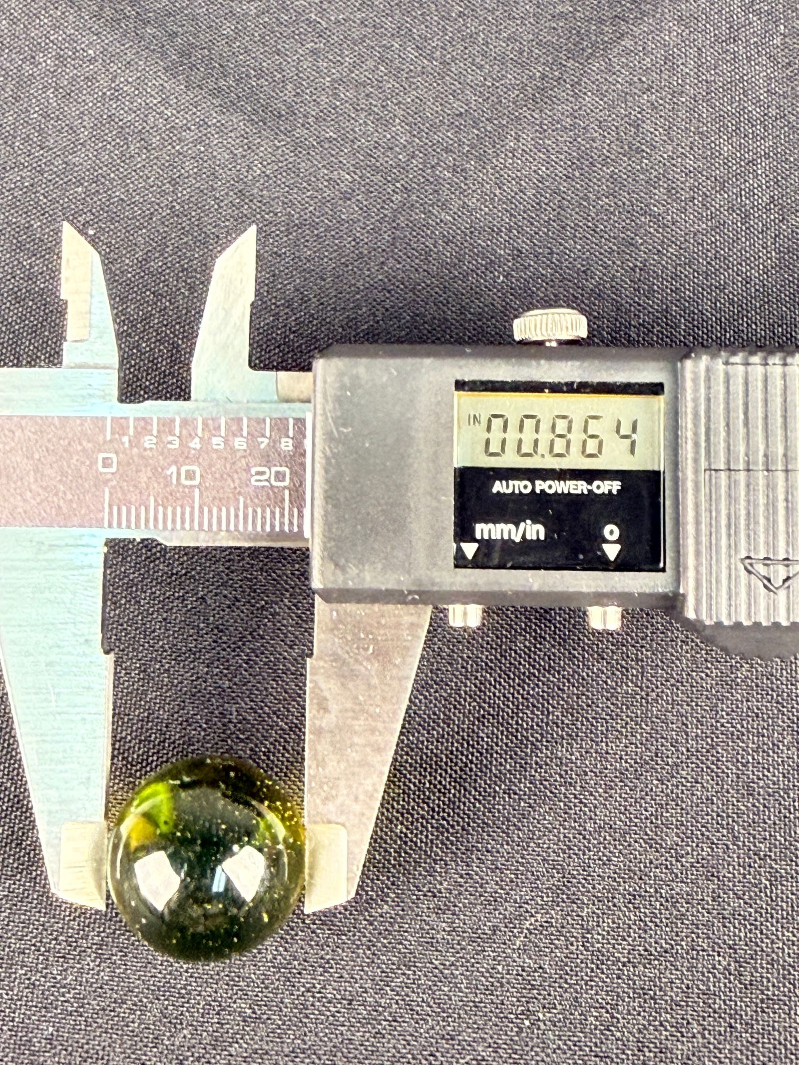 A Vintage Uranium Marble Shooter: The translucent yellowish-green sphere features internal seeds and a distinct yellow swirl or patch. The item exhibits a strong, bright green fluorescence when subjected to ultraviolet light. Diameter