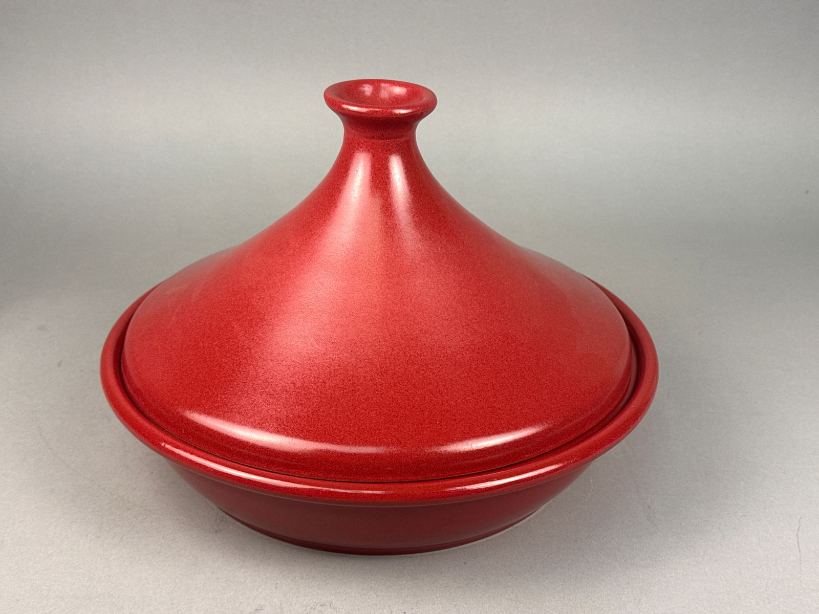 Emile Henry France Flame Red Ceramic Tagine: An Emile Henry Flame red ceramic tagine manufactured in France. The two-piece cooking vessel consists of a shallow circular base and a tall conical lid with a knob handle. The piece is finished in a r