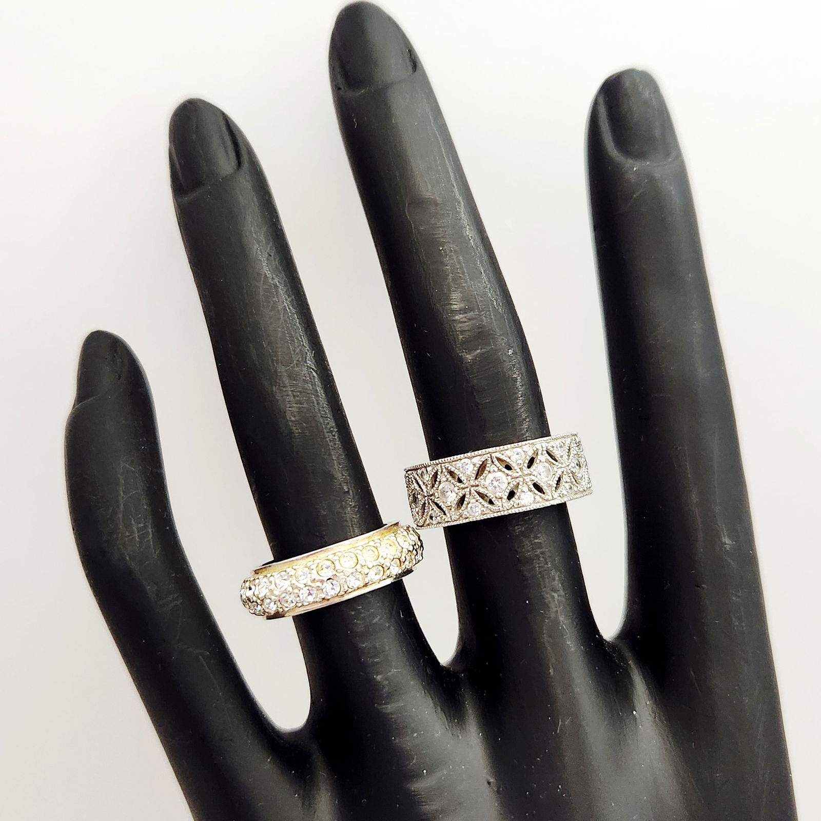 Sterling Cubic Zirconia Rings 10.7 Grams: This lot consists of two sterling silver band rings. The first ring is a wide band featuring an intricate filigree design set with clear stones; the interior is stamped CZ 925 and CHINA. The second ri