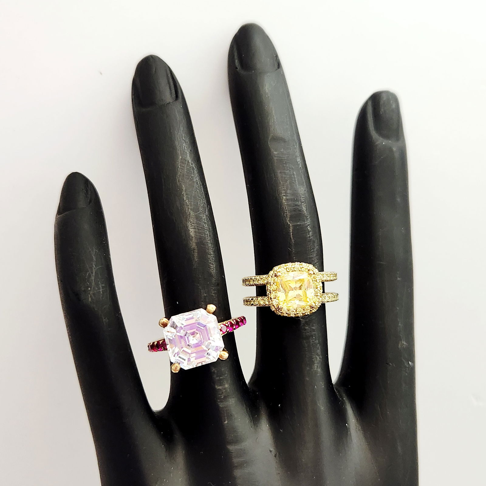 Vermeil Cubic Zirconia Rings 10.1 Grams: Two gold over sterling (vermiel) rings featuring cubic zirconia stones. The first ring is designed with a central emerald-cut clear cubic zirconia flanked by rows of small, round-cut red cz stones. Th