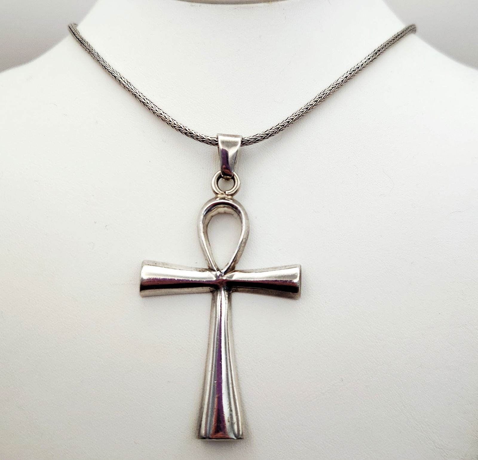 Ketut Suarti Sterling Ankh Necklace 39 Grams: A sterling silver necklace featuring an Egyptian-style ankh pendant by designer Ketut Suarti. The pendant features a polished finish and flared ends. It is suspended from a braided wheat-style chain