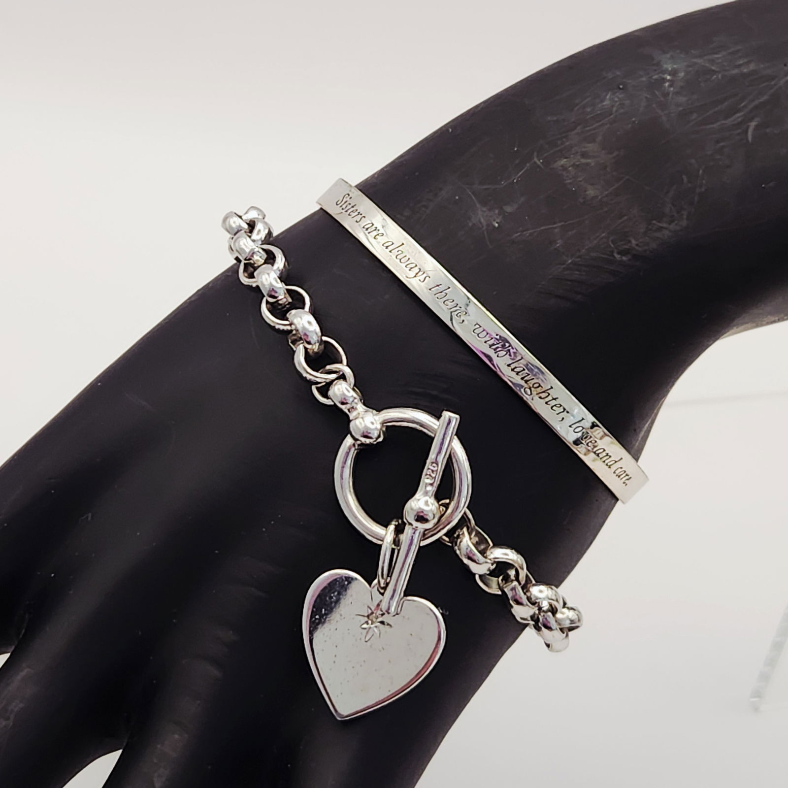 Two Sterling Bracelets 26.4 Grams: This lot features two sterling silver bracelets. The first is a round-link chain bracelet with a toggle clasp hallmarked 925. Attached to the clasp is a heart-shaped charm featuring a small star-set c