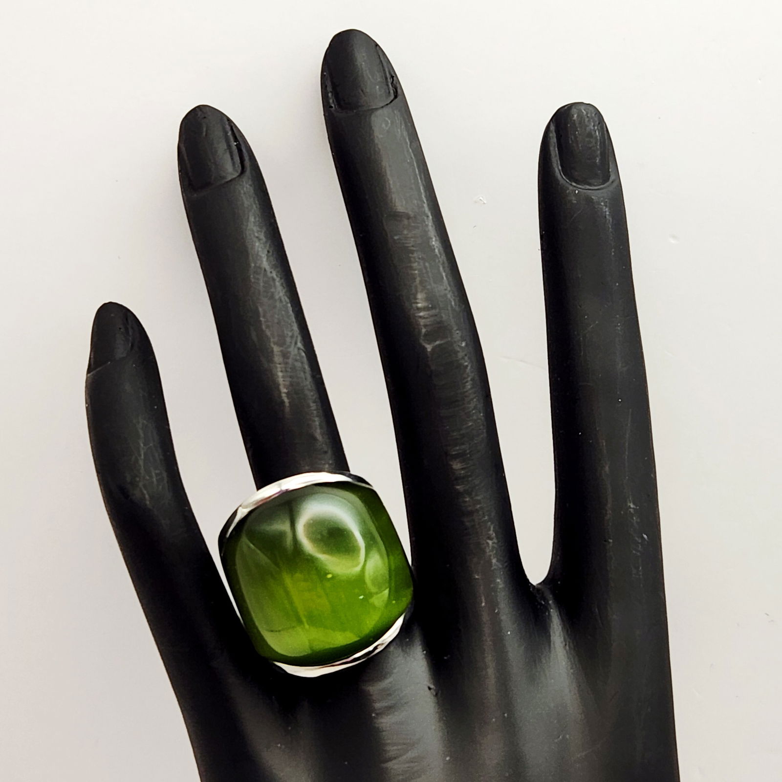 Sterling Green Cabochon Stone Ring 20.7 Grams: This modern silver-toned cocktail ring features a large, translucent green cabochon stone in a square cushion cut. The stone is securely set within a wide, polished band. The underside of the setting