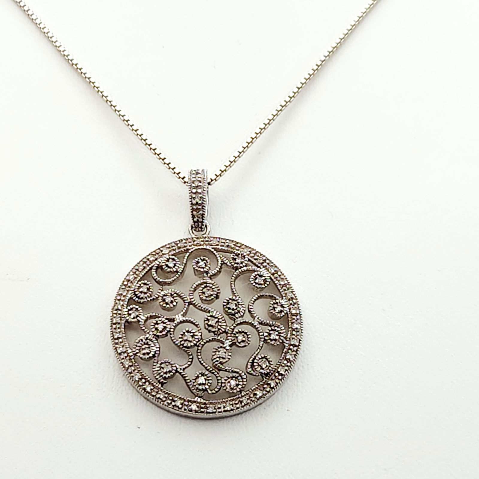 Sterling Diamond Filigree Necklace 8.2 Grams: A sterling silver accent diamonds filigree pendant necklace. The circular openwork pendant features an intricate scrolling filigree design accented with multiple small round-cut diamonds. The pendant