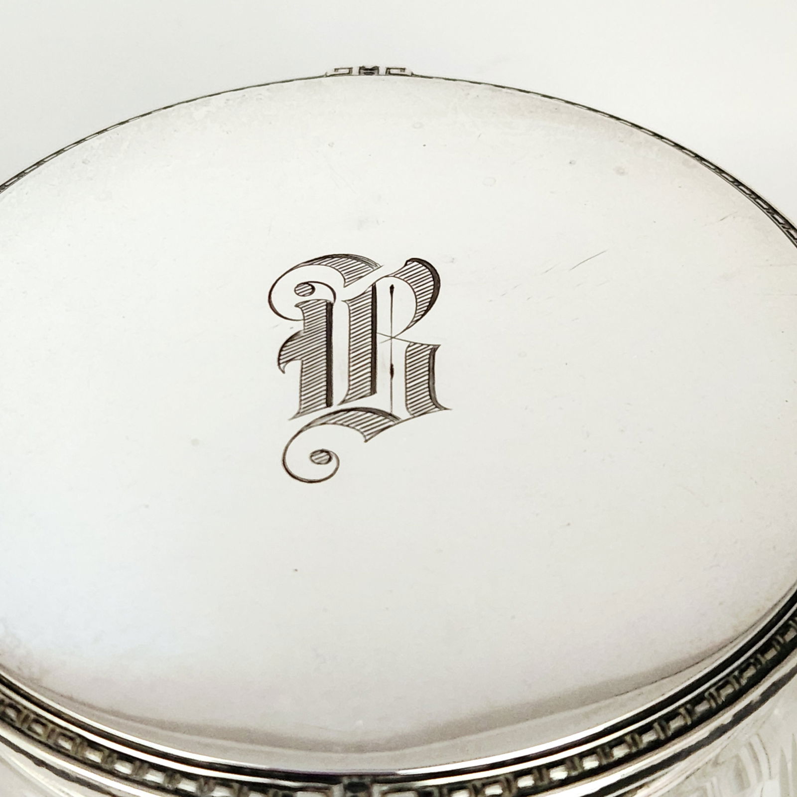 Sterling Mounted Dresser Jar 3.8 Ounces: A sterling silver mounted cut glass dresser jar. The circular glass base is decorated with vertical fluting and geometric cut patterns. The sterling silver lid features a patterned border and a centra