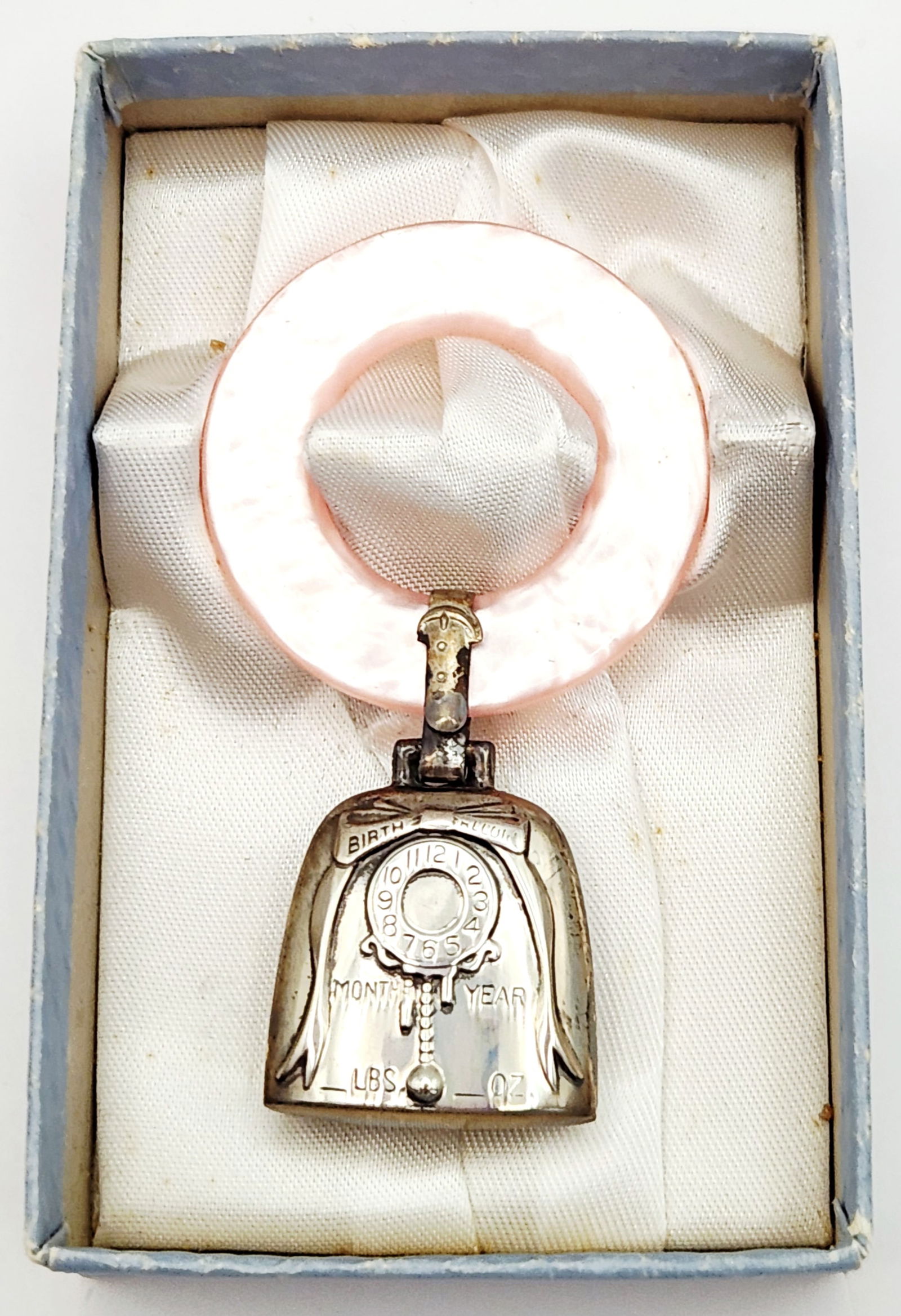 Web Sterling Birth Record Teething Ring 13 Grams: This mid-century baby teething ring by Web Sterling features a pink pearlescent ring connected to a sterling silver bell-shaped birth record pendant. The front of the bell is embossed with BIRTH RECOR