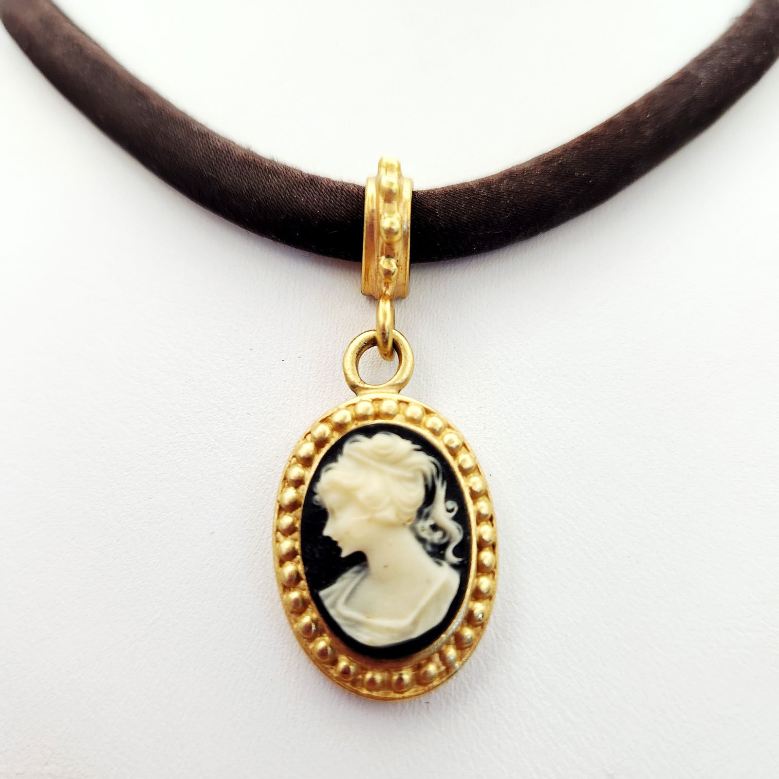 Carolee Gold-Tone Black Satin Cameo Choker Necklace: This choker necklace features a black satin-finish cord adorned with an oval cameo pendant. The pendant depicts a classically styled female profile in relief against a black ground, encased in a gold-