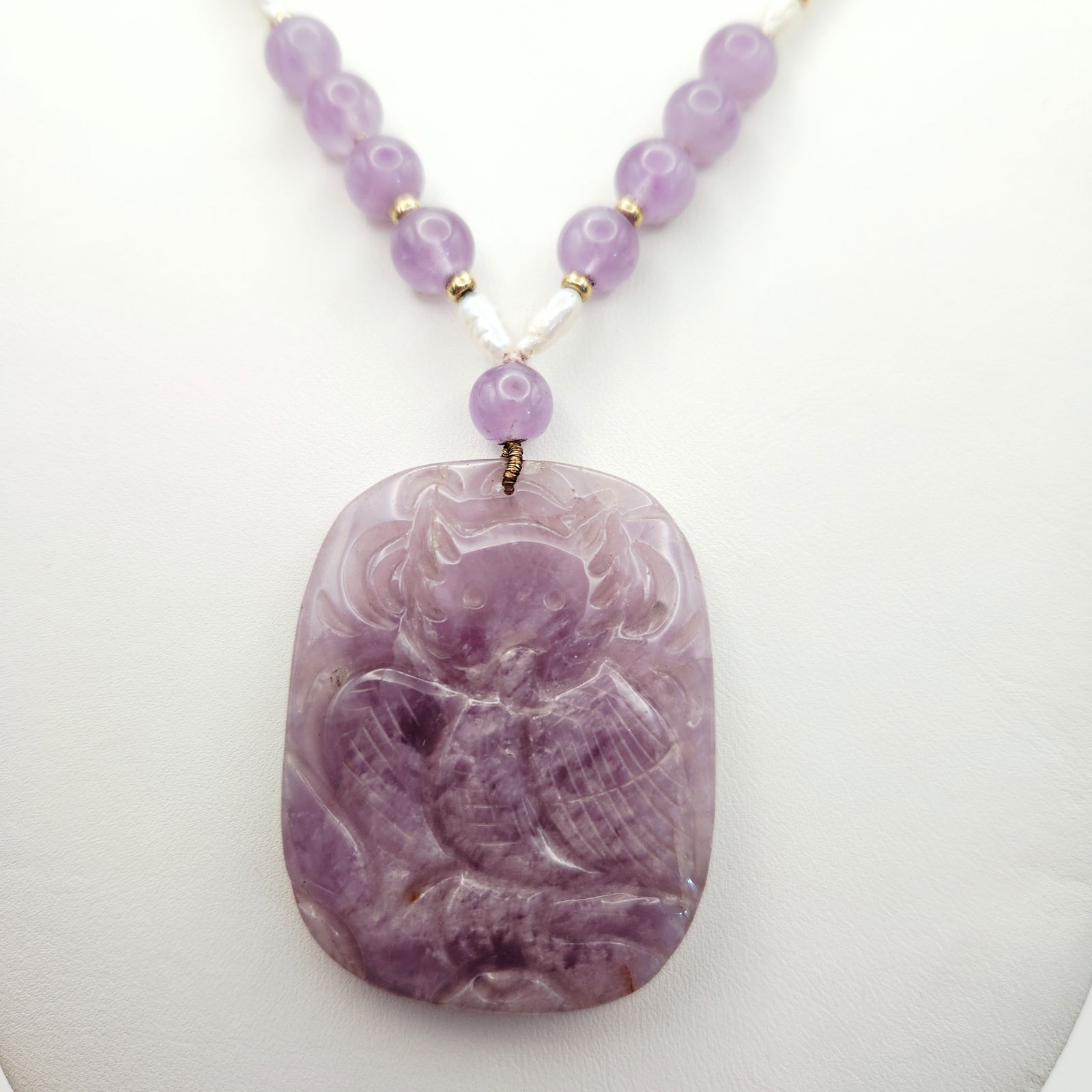 Carved Amethyst & Pearl Beaded Necklace: This necklace features a large, oval-shaped carved amethyst pendant depicting a Owl and floral motifs. The strand is composed of round amethyst beads, small white pearls, and gold-tone spacer beads. A
