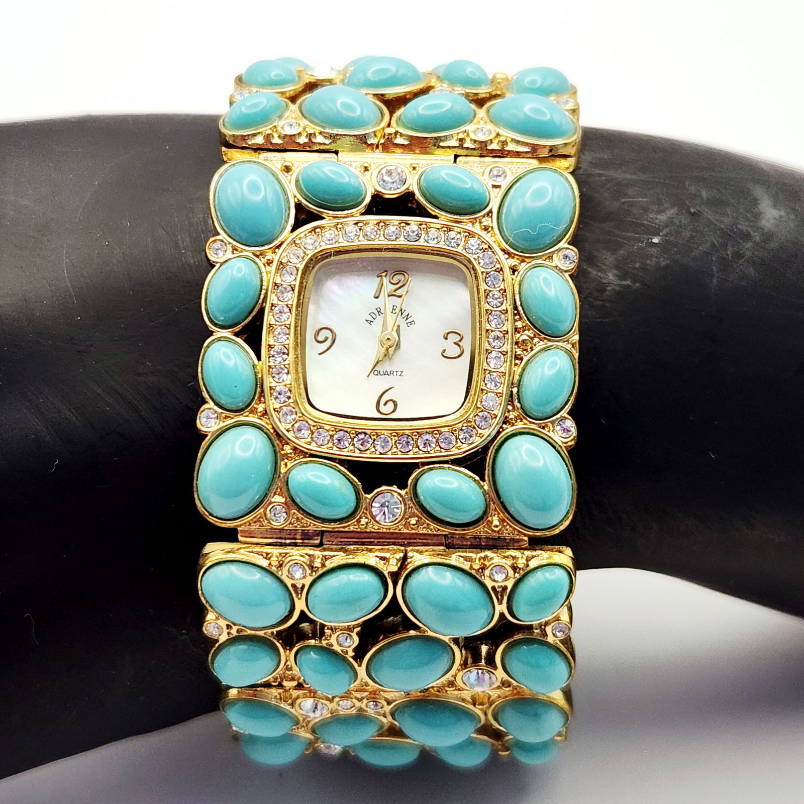 Adrienne Gold-Toned Ladies Watch Turquoise-Colored Cabochons: An Adrienne brand ladies fashion wrist watch featuring a wide gold-toned link band embellished with multiple oval turquoise-colored cabochons and clear rhinestone accents. The watch is constructed wit
