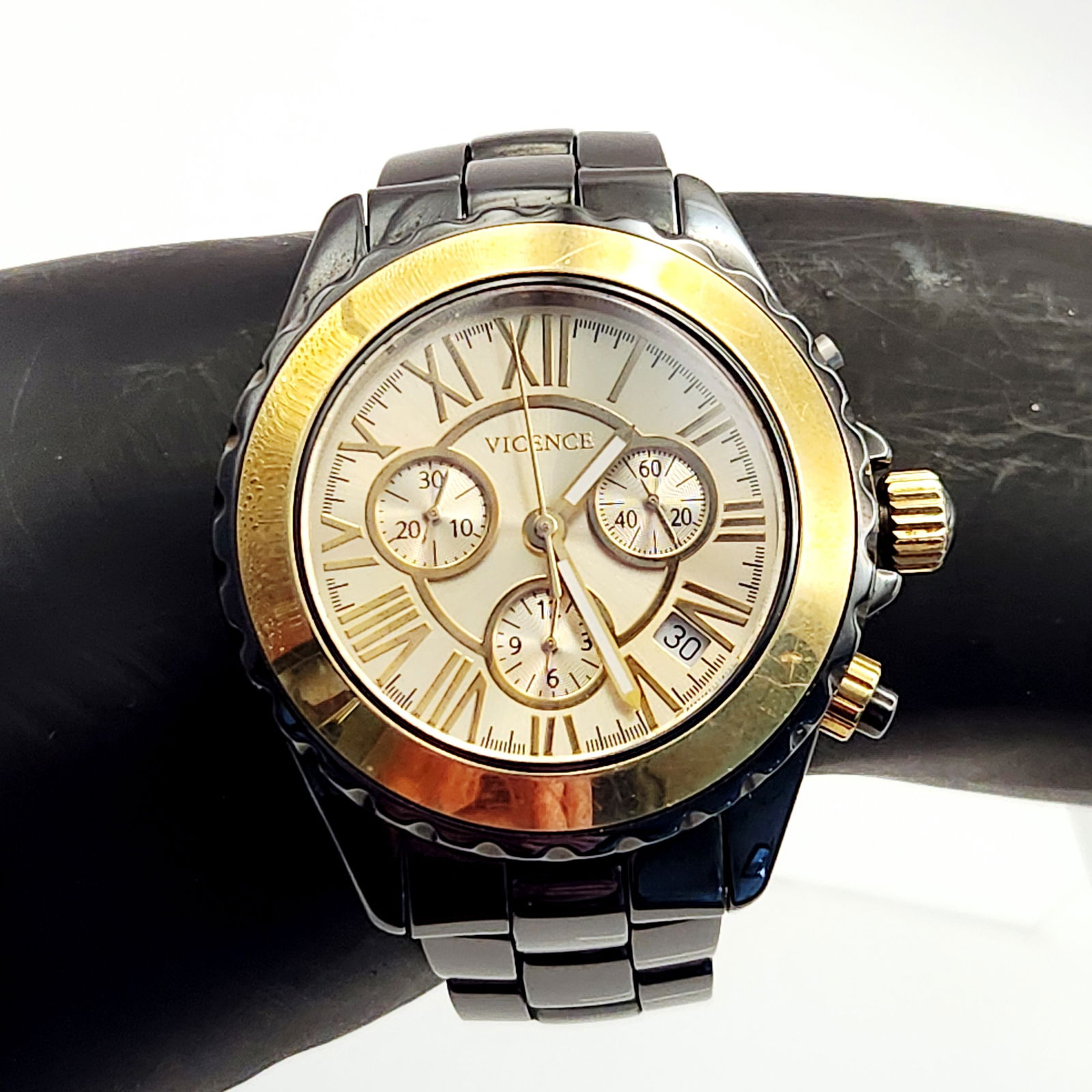 Vicence 14KT Gold Bezel Chronograph Wristwatch #V39115692: A Vicence chronograph wristwatch featuring a two-tone design. The timepiece is constructed with a 14kt yellow gold bezel set on a black-finished case. The light-toned dial is detailed with Roman numer