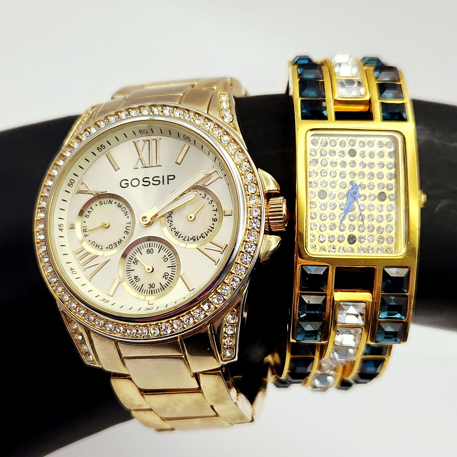 Gold-Tone Gossip & Adrienne Couture Quartz Watches: A group of two contemporary gold-tone wristwatches. The first is a Gossip model GSP860 featuring a round case with a crystal-encrusted bezel and lugs. The dial includes three sub-dials for day, date,
