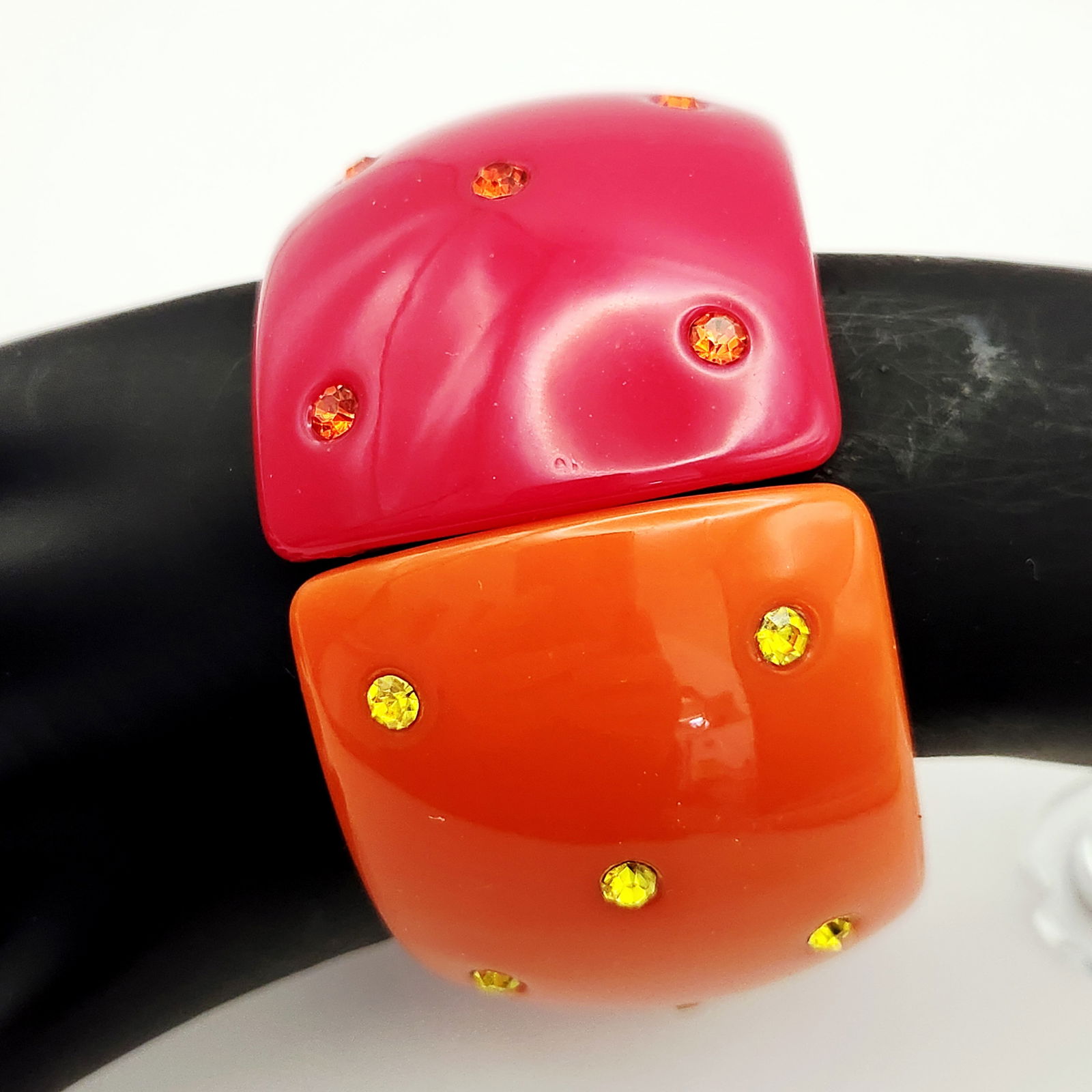 Two-Tone Resin and Crystal Hinged Cuff Bracelet: A wide, two-tone hinged cuff bracelet crafted from glossy resin. The domed form is divided into two distinct color halves: magenta-pink and orange. Both sections feature inset, round faceted crystals