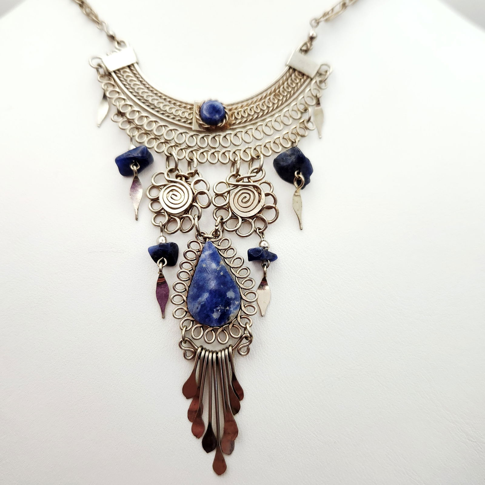 A Silver-Tone Wirework & Sodalite Ethnic Style Bib Necklace: A bib necklace of ethnic design featuring intricate silver-tone wirework construction. The central decorative section is composed of layered scrollwork, circular motifs with spiral centers, and variou