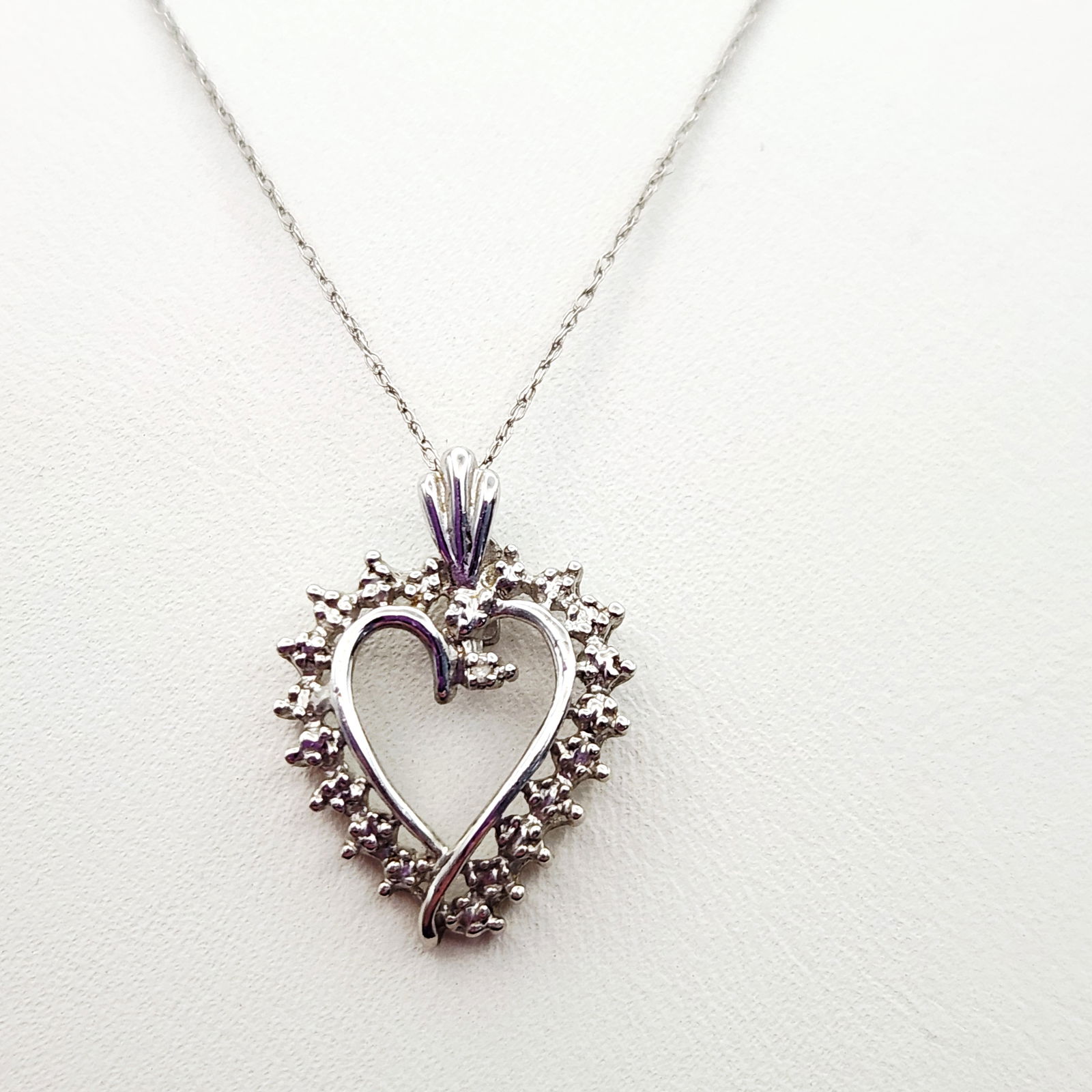 10K White Gold Heart Necklace 1.7 Grams: This necklace features a heart-shaped pendant crafted in 10K white gold, designed with an open center and an internal scroll motif. The pendant is bordered by numerous small, round-cut clear stones