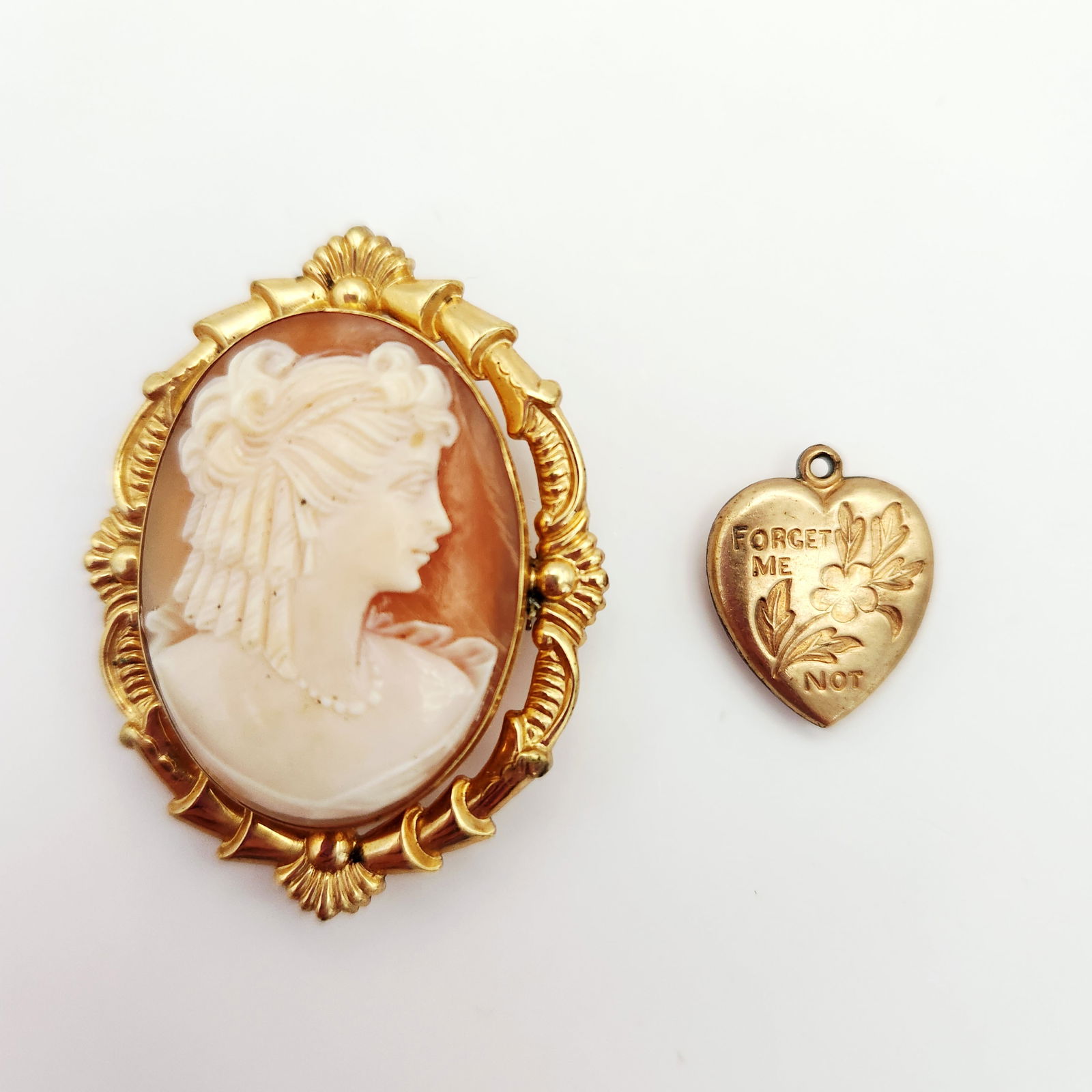 12K Gold-Filled Cameo & Pendant 7.5 Grams: This lot consists of two jewelry items made of 1/20 12K gold-filled metal. The first item is an oval brooch featuring a carved shell cameo depicting a female profile. The shell is set in an ornate gol