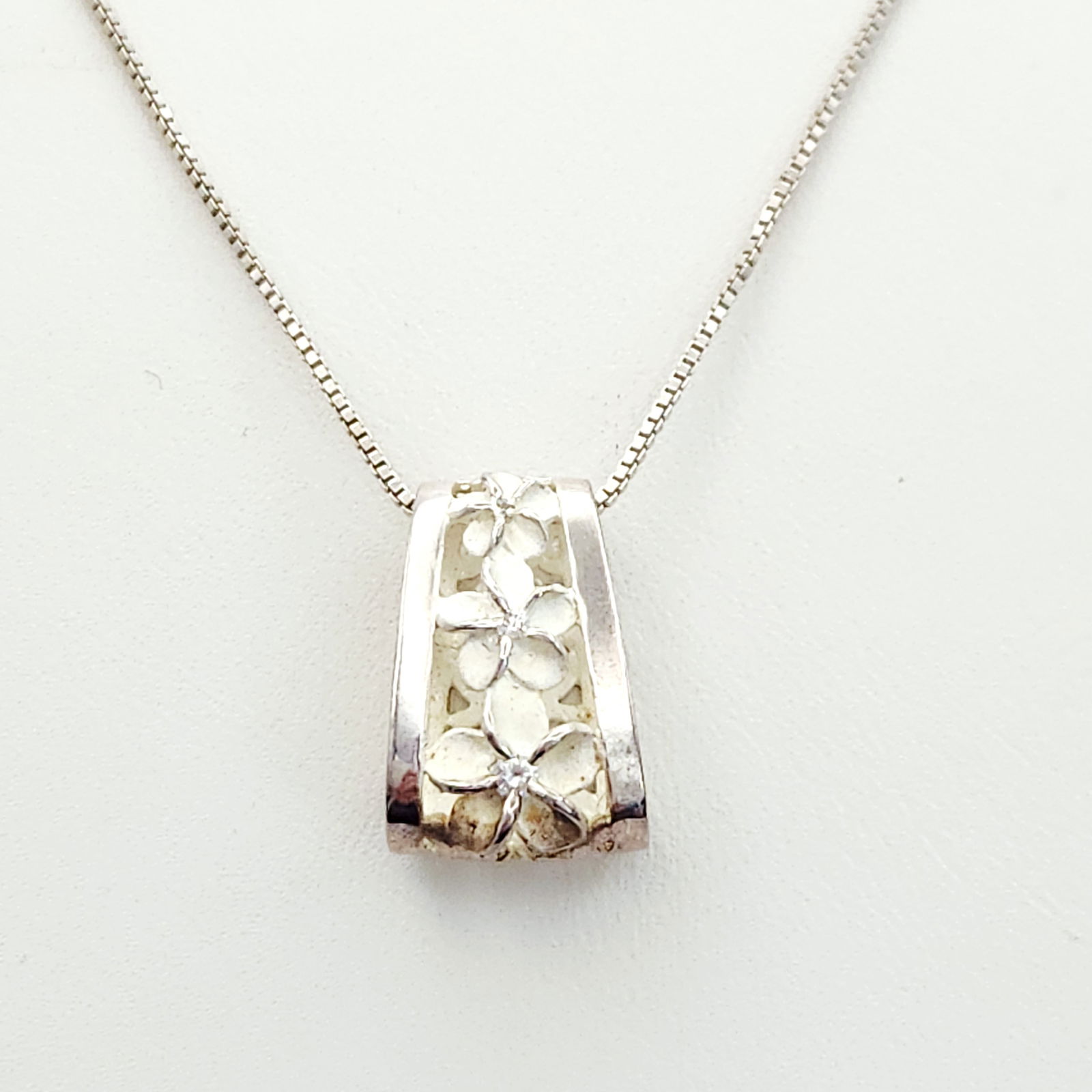 Sterling Plumeria Slider Necklace 4.6 Grams: This sterling silver necklace features a wide, curved slider pendant decorated with three plumeria blossoms. The blossoms are accented by white enamel or shell inlay. The pendant exhibits openwork