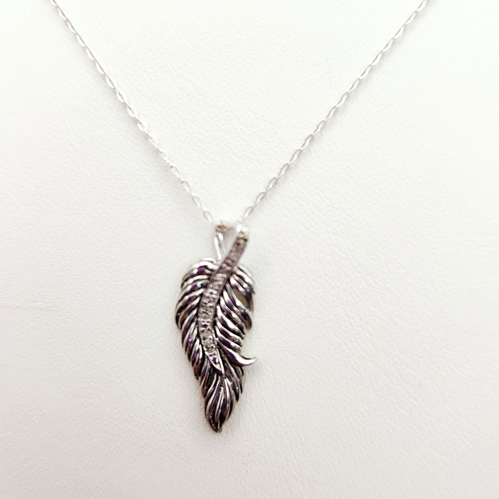 Sterling Feather Pendant Necklace 2 Grams: A contemporary sterling silver necklace featuring a feather-shaped pendant. The pendant is decorated with a center row of small, round-cut clear stones. The reverse of the pendant bears the hallmark