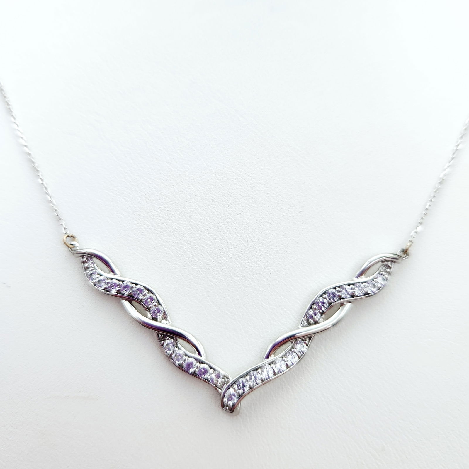 Sterling Chevron Pendant Necklace 5.3 Grams: A sterling silver necklace featuring a chevron-style pendant with a twisted, openwork design. The pendant is accented by clear faceted stones. The reverse of the pendant is marked SUN and 925. The