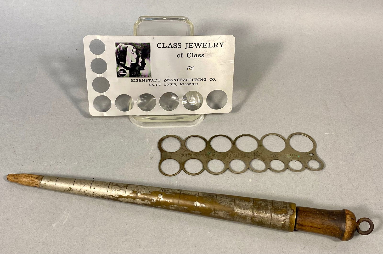 A Trio of Vintage Jewelry Sizing Tools: A collection of three vintage jewelry sizing instruments. The first is a rectangular metal ring sizing card produced by the Eisenstadt Manufacturing Co. of St. Louis, Missouri. The card features sizin