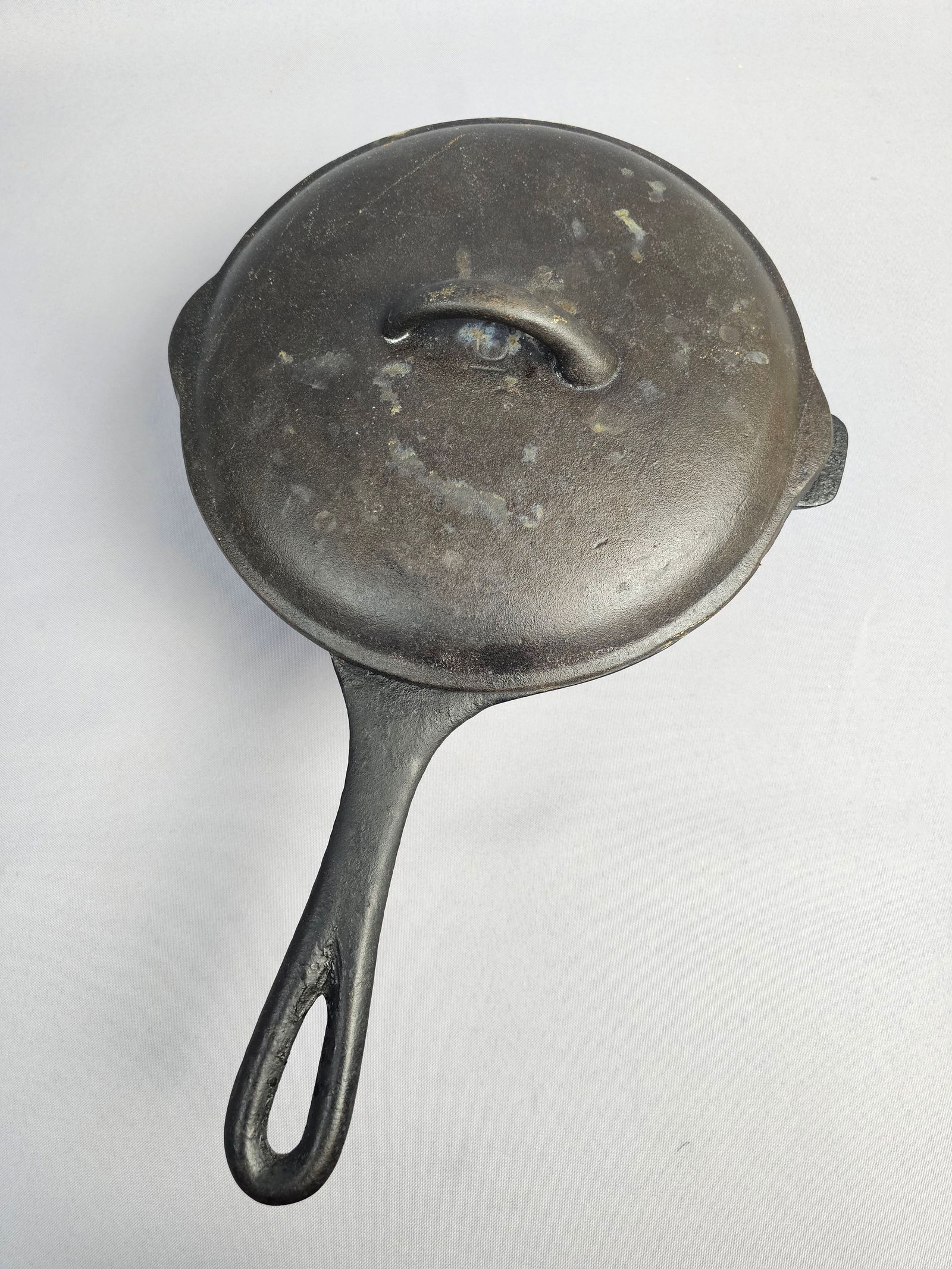 Vintage Lidded Cast Iron 3 qt Sauce Pot: A Bayou Classic covered cast iron sauce pot. This heavy-duty cookware features a deep, straight-sided vessel with an integral long handle and a small helper tab on the opposite rim. The matching