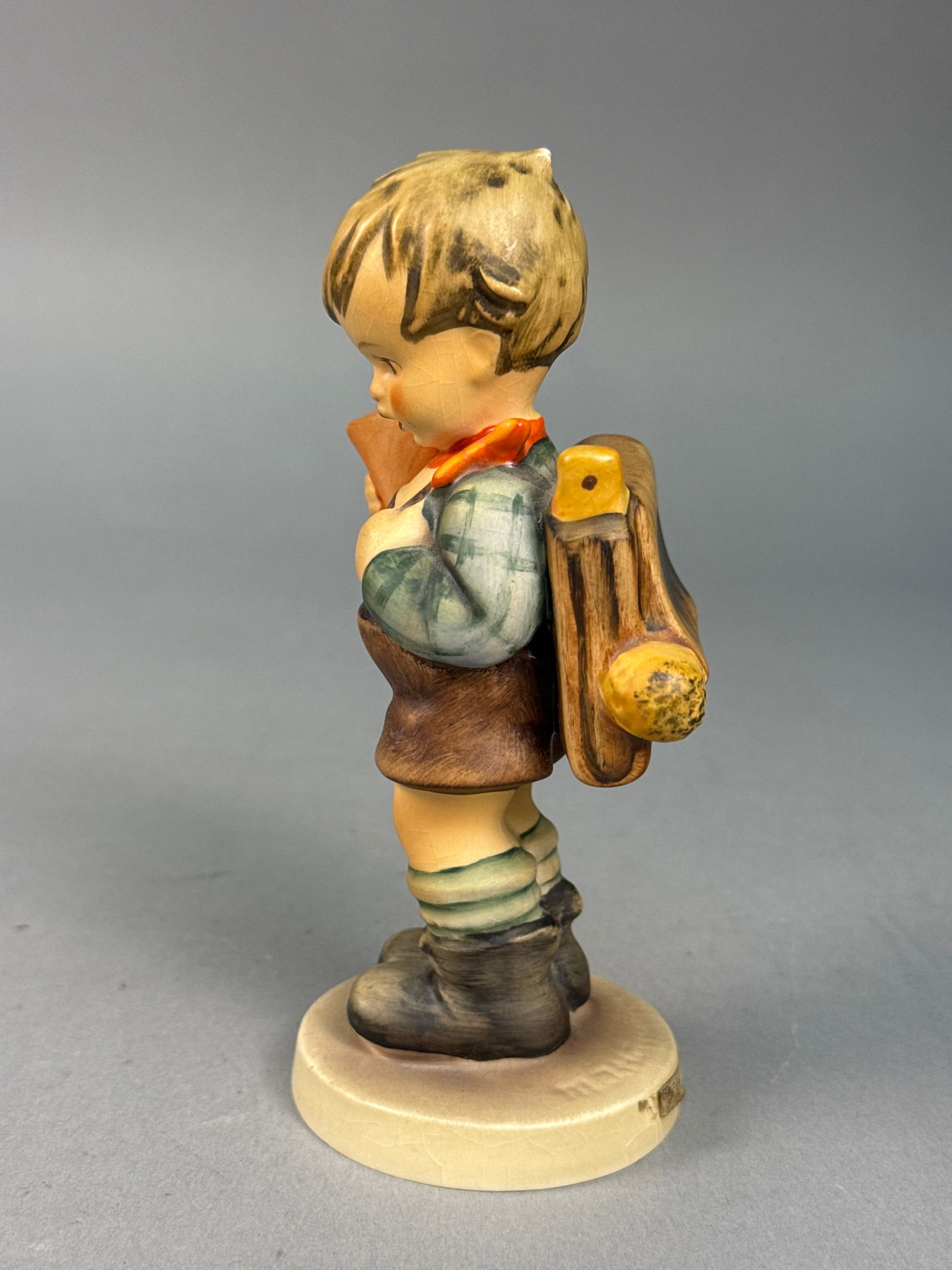 Goebel Hummel Little Scholar Figurine Number 80 TMK3: A Goebel Hummel hand-painted porcelain figurine titled Little Scholar, model number 80. T The figurine is set upon a circular cream-colored base. The underside is marked with a blue Goebel W. Germany