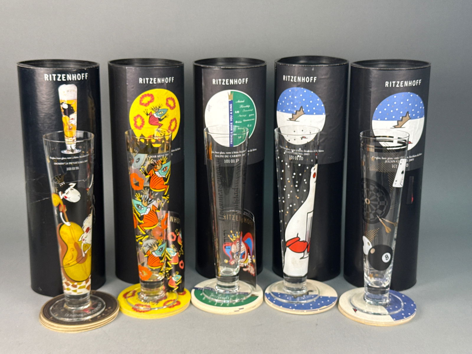 A Collection of Ritzenhoff Designer Beer Glasses: A collection of contemporary designer pilsner beer glasses by Ritzenhoff, featuring various whimsical graphic motifs. The group includes designs by several artists, such as a 2001 music-themed glass b