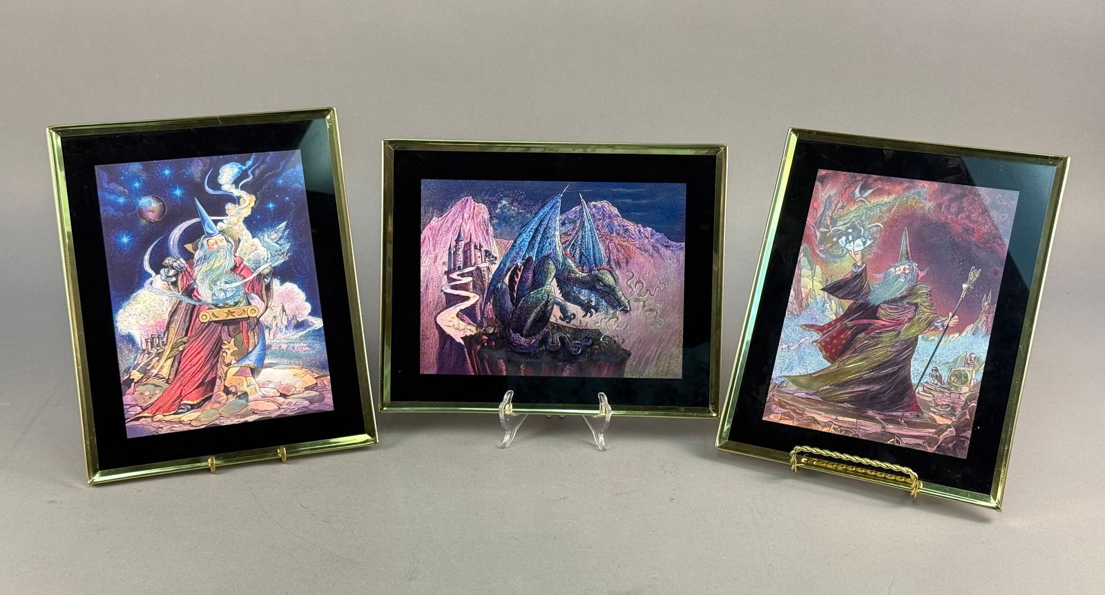 A Trio of Framed Fantasy Art Prints by Judy Mastrangelo: A trio of illustrative fantasy-themed art prints by Judy Mastrangelo. The collection includes three distinct works titled on the reverse as Wizard & Magic Crystal, Blue Dragon-Purple Cliff, and Wi