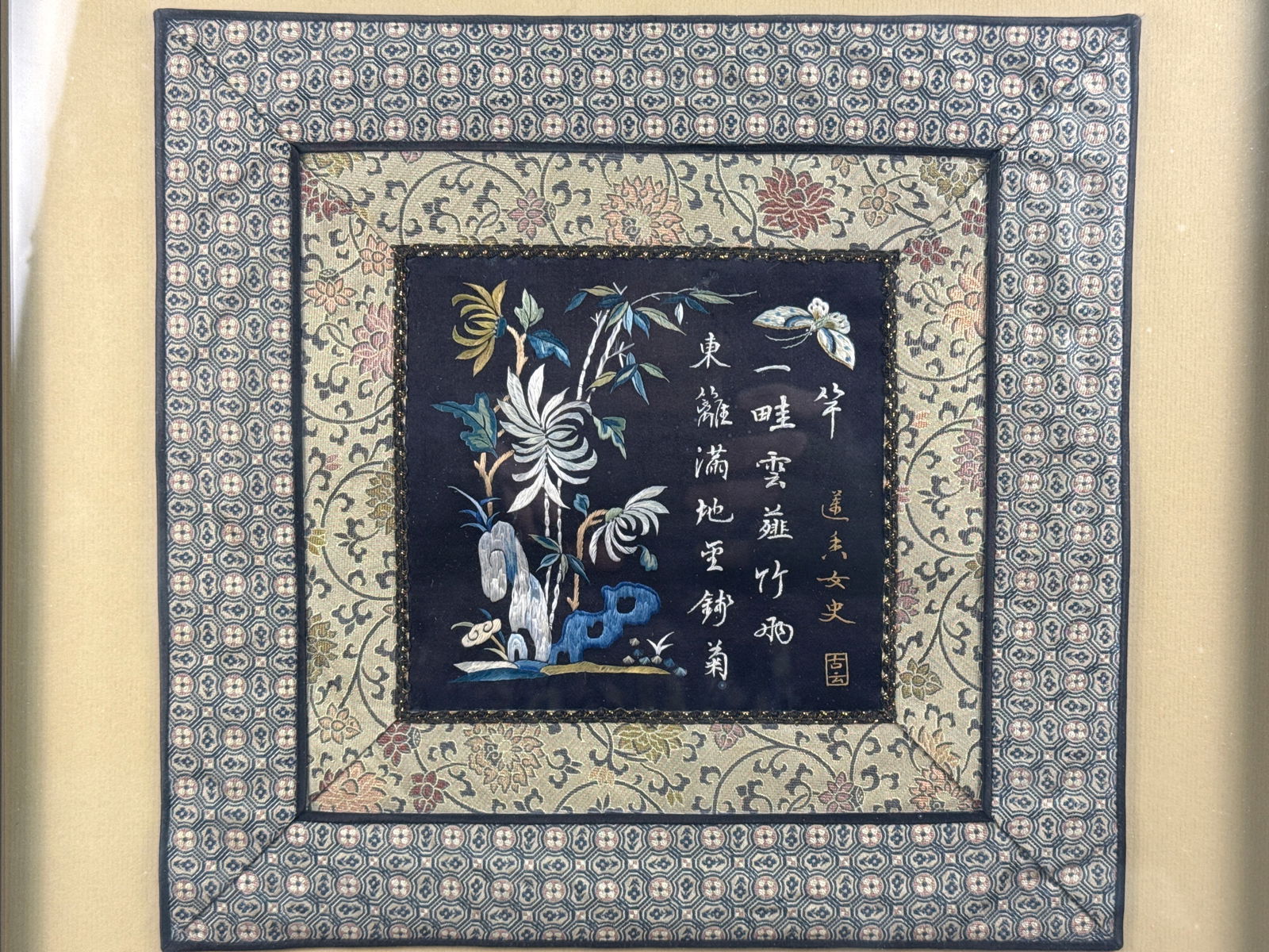 A Framed Chinese Silk Embroidery Panel: This Chinese silk embroidery panel features a central square of dark silk ground with polychrome silk thread embroidery. The central scene depicts a flowering chrysanthemum, a scholar's rock, and a bu