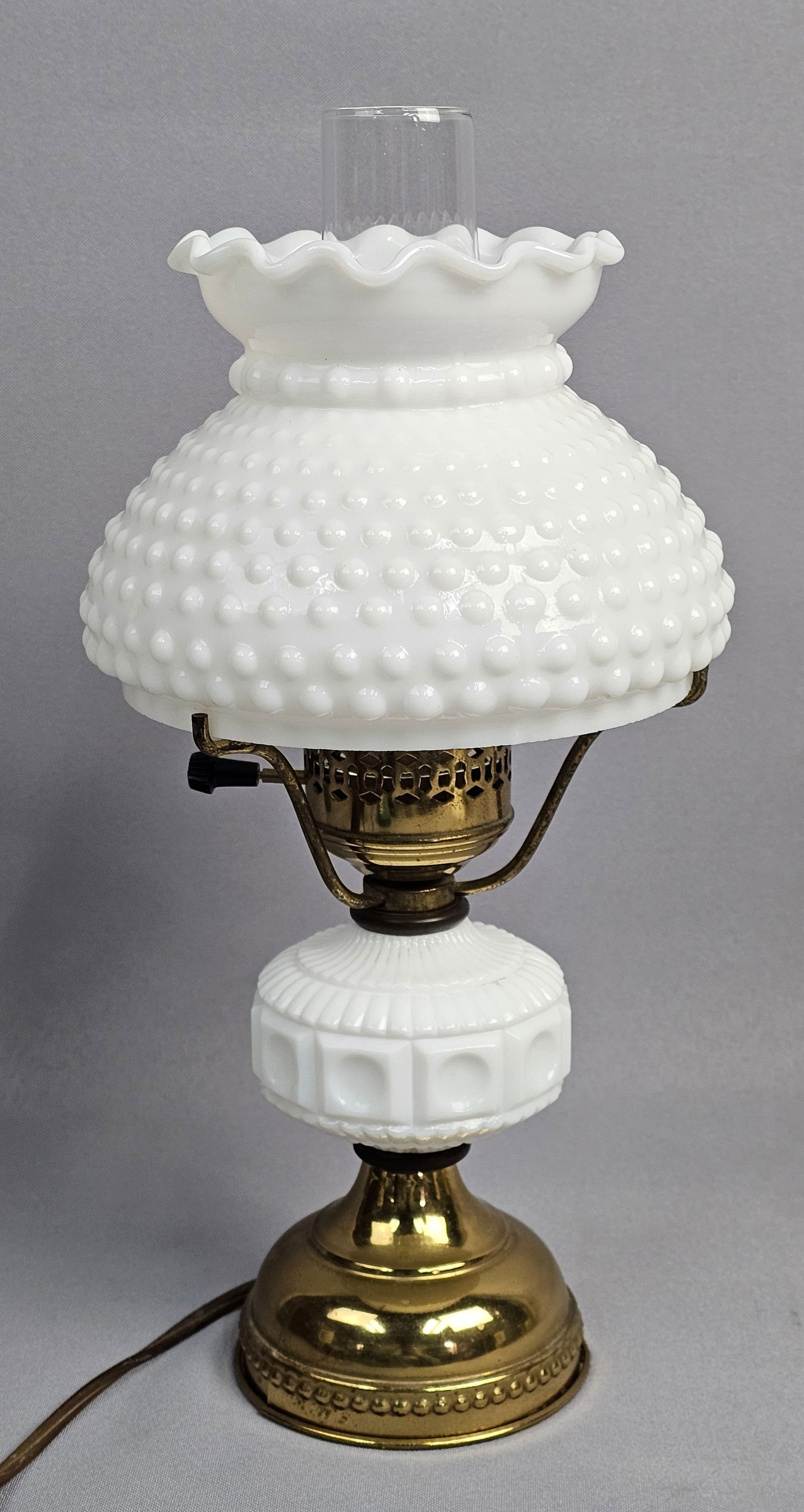 Vintage White Hobnail Milk Glass Table Lamp: This vintage electric table lamp features a white hobnail milk glass shade with a ruffled top edge and a clear glass interior chimney. The central font is crafted from white milk glass with a molded g