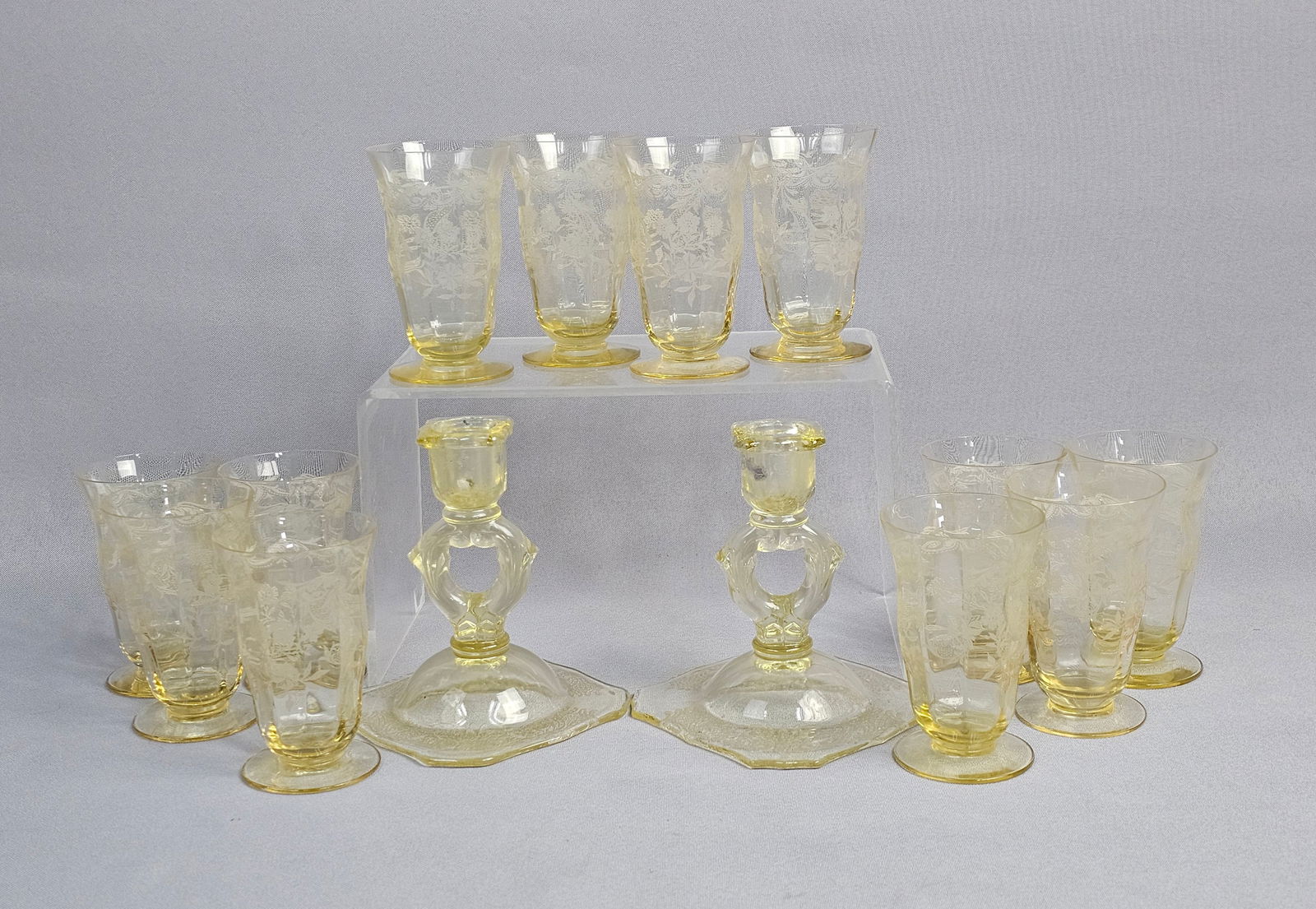 A Collection of Vintage Yellow Glass Tableware: The group consists of a pair of candlesticks and multiple footed tumblers. Each piece features an intricate etched design consisting of floral motifs and scrollwork. The candlesticks are designed with